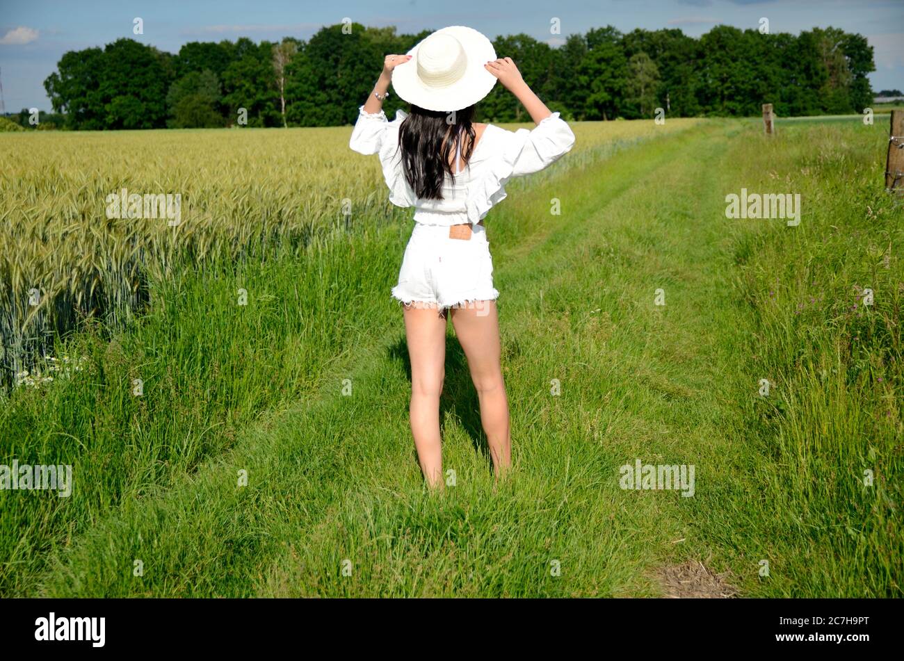 Une fille pieds nus marchant sur l'herbe verte. Femme avec chapeau, short blanc et haut blanc. Été en Pologne, belle terre agricole en Basse Silésie. Banque D'Images