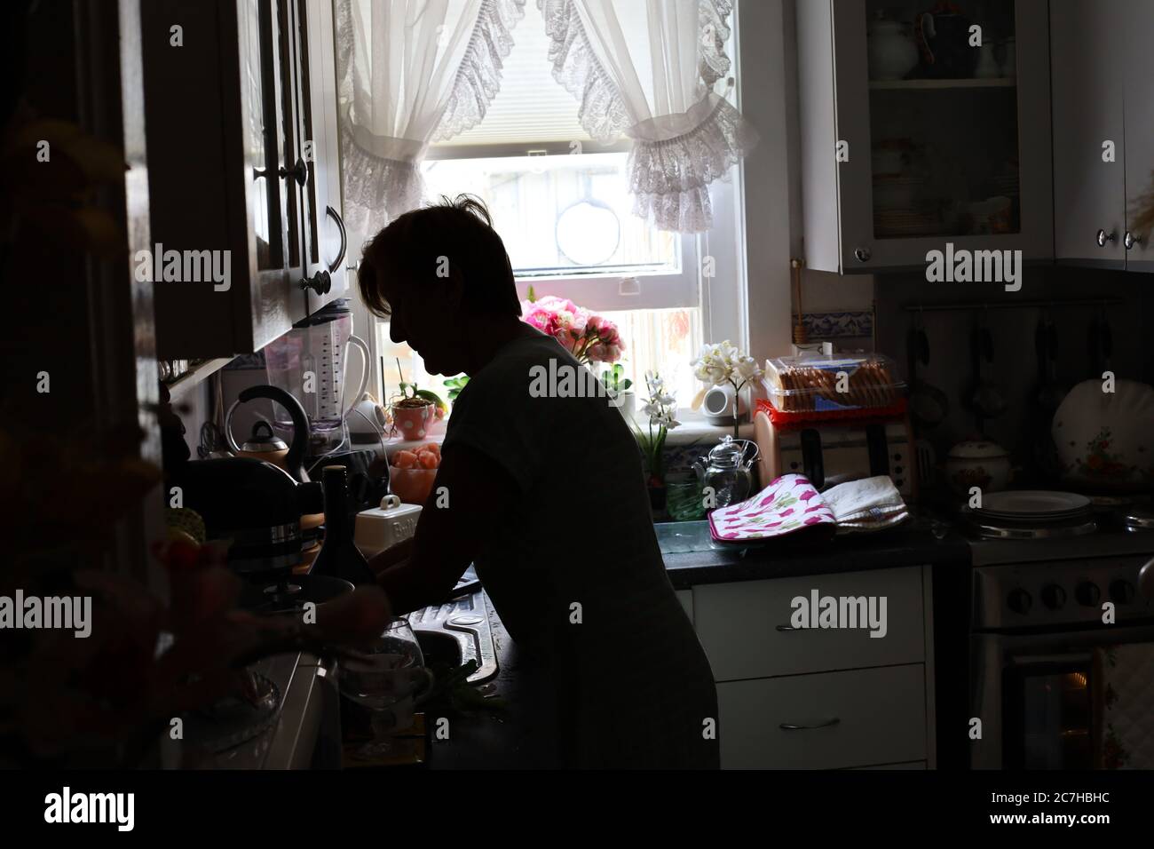 Silhouette d'une femme préparant la nourriture dans la cuisine avec lumière du soleil provenant de la fenêtre Banque D'Images