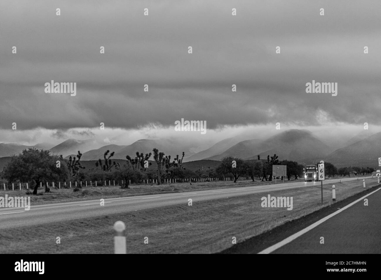 Prise de vue en niveaux de gris d'une route avec des montagnes au loin sous un ciel nuageux Banque D'Images