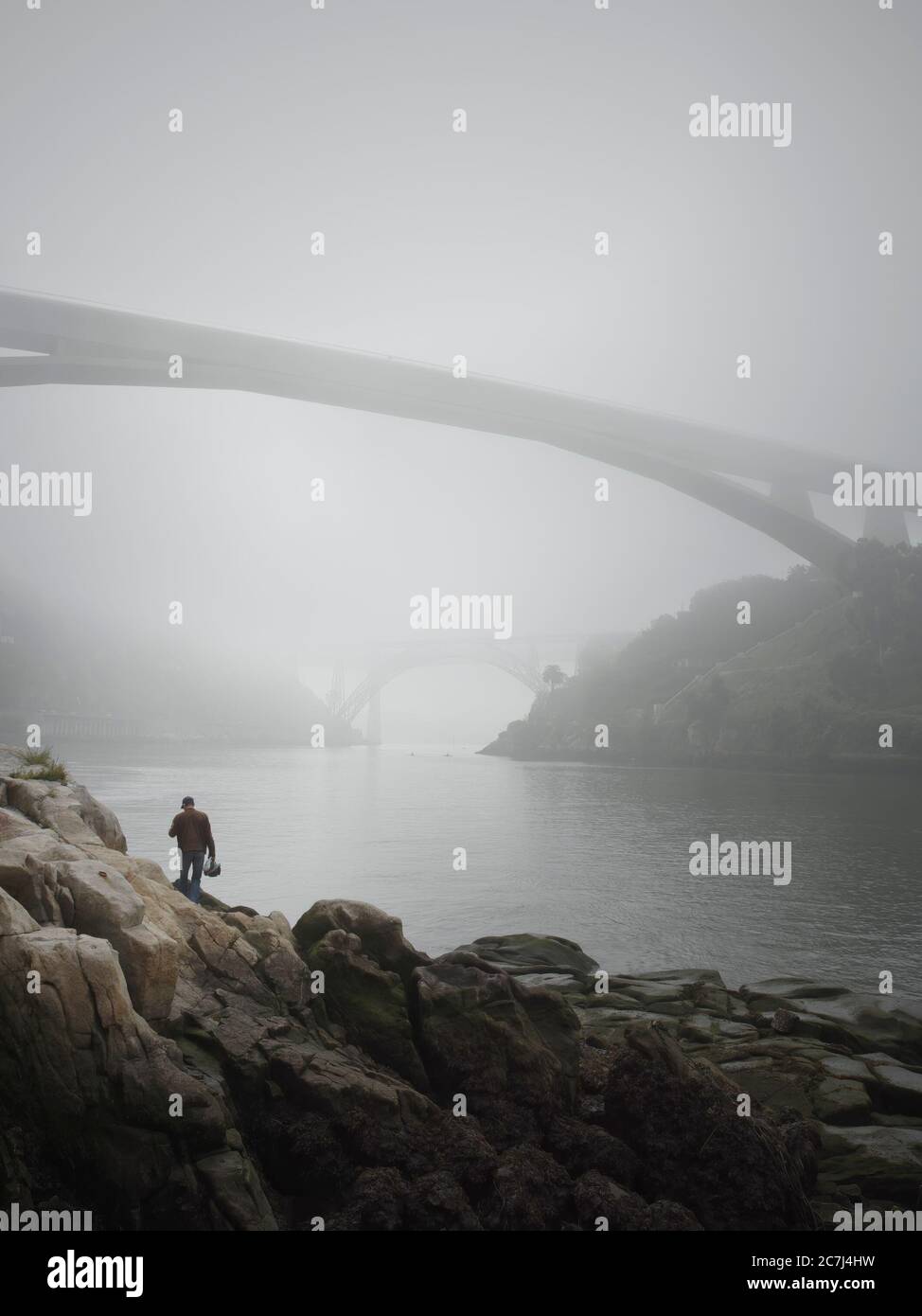 Porto, Portugal - 25 avril 2006 : l'homme seul sur la rive du Douro, voyant deux des ponts célèbres et magnifiques de Porto dans le brouillard du matin. Banque D'Images