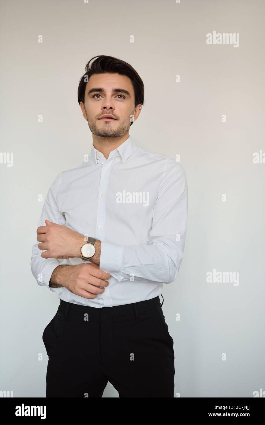 Jeune homme élégant de brunette en chemise blanche et pantalon noir avec  montre à main, regardant de côté sur fond blanc seul Photo Stock - Alamy