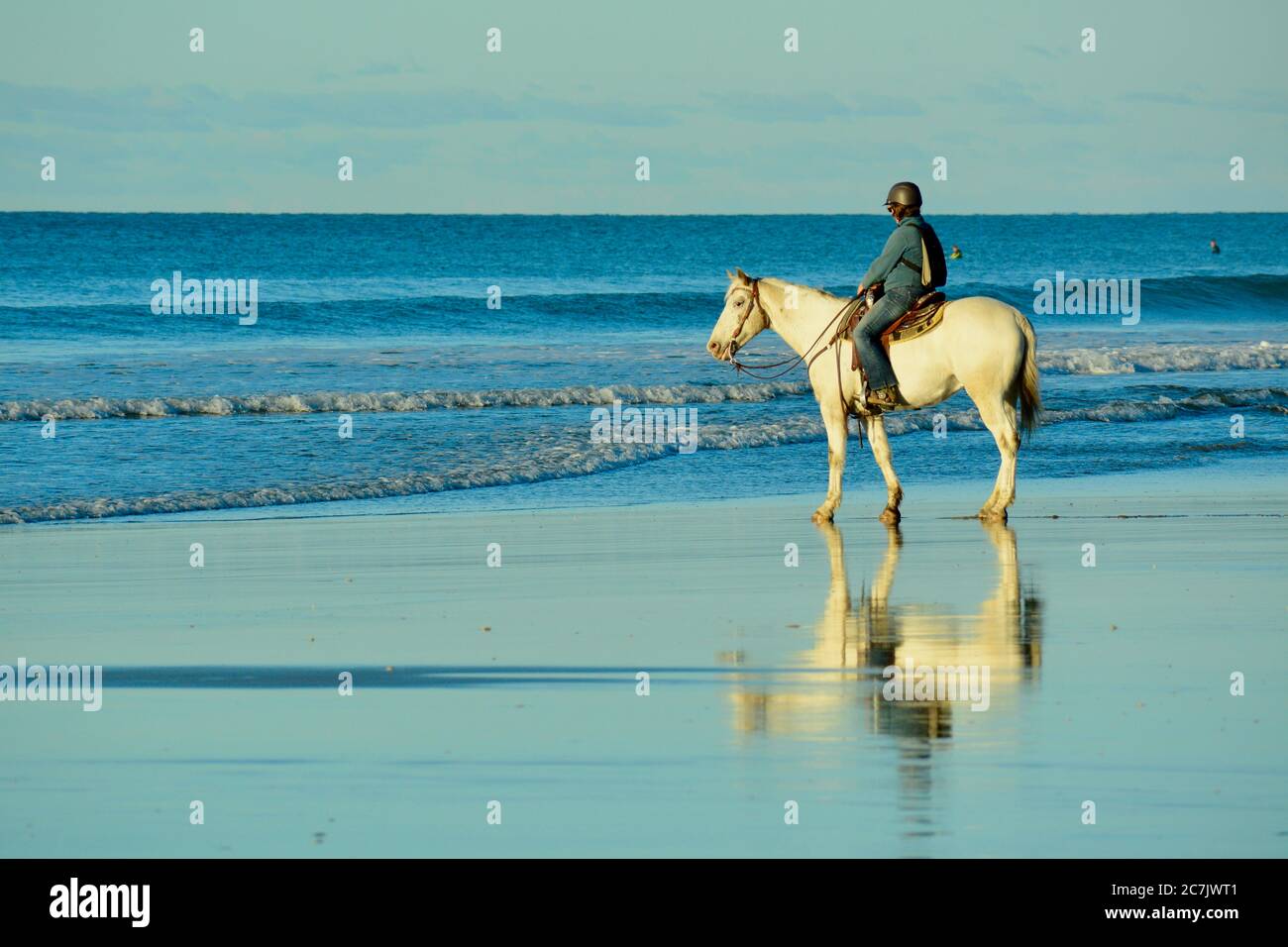 Plage de Papamoa, Papamoa, Nouvelle-Zélande – 07 juillet 2019 : une femme non identifiée sur un cheval blanc à bord d'un rivage. Banque D'Images
