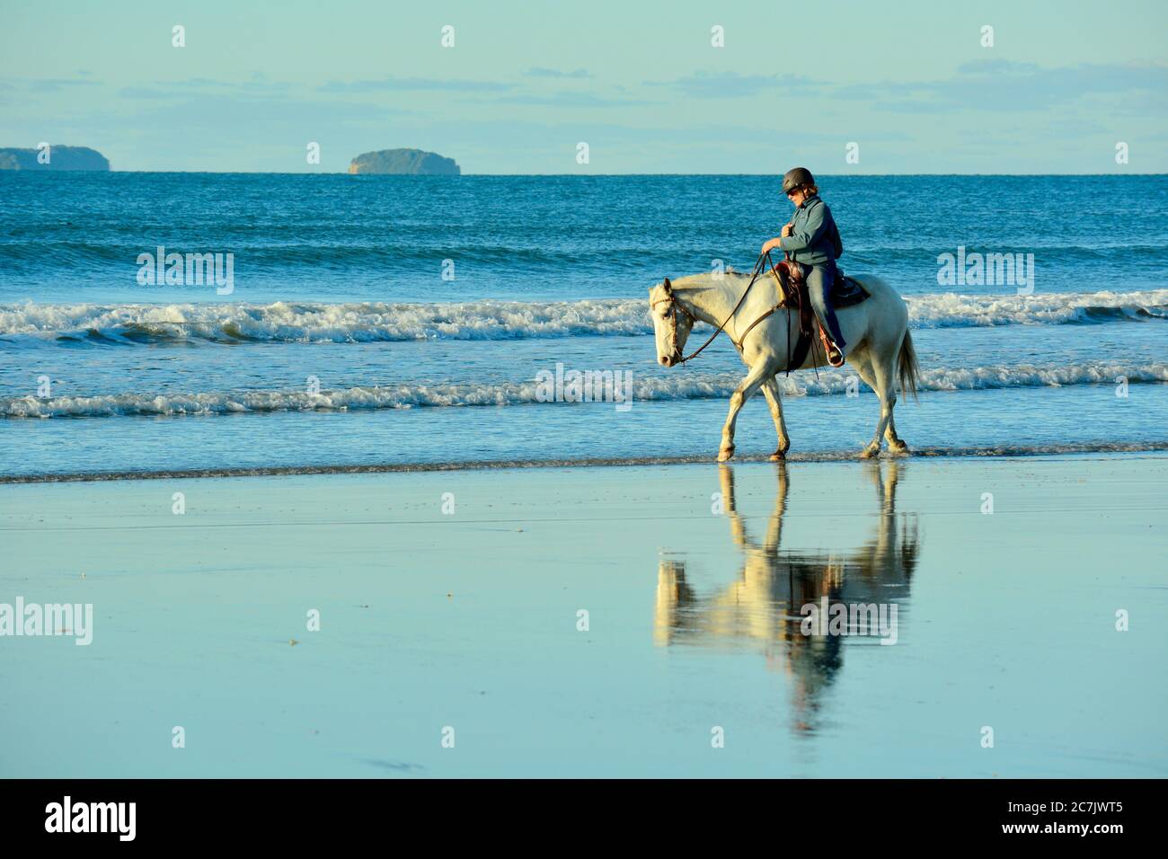 Plage de Papamoa, Papamoa, Nouvelle-Zélande – 07 juillet 2019 : une femme non identifiée sur un cheval blanc à bord d'un rivage. Banque D'Images