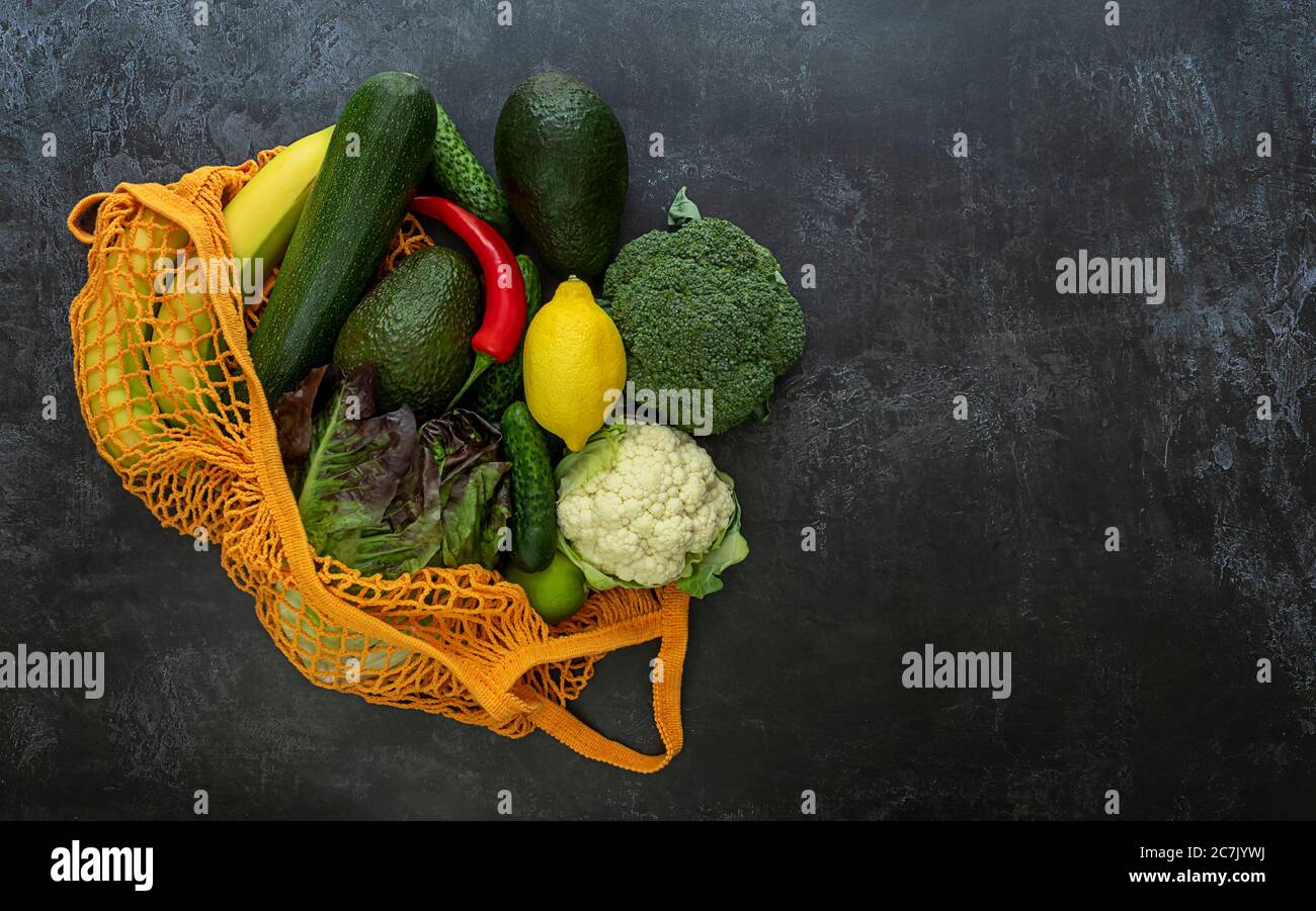 Légumes et fruits mûrs dans un sac à ficelle d'orange sur fond sombre. Banque D'Images