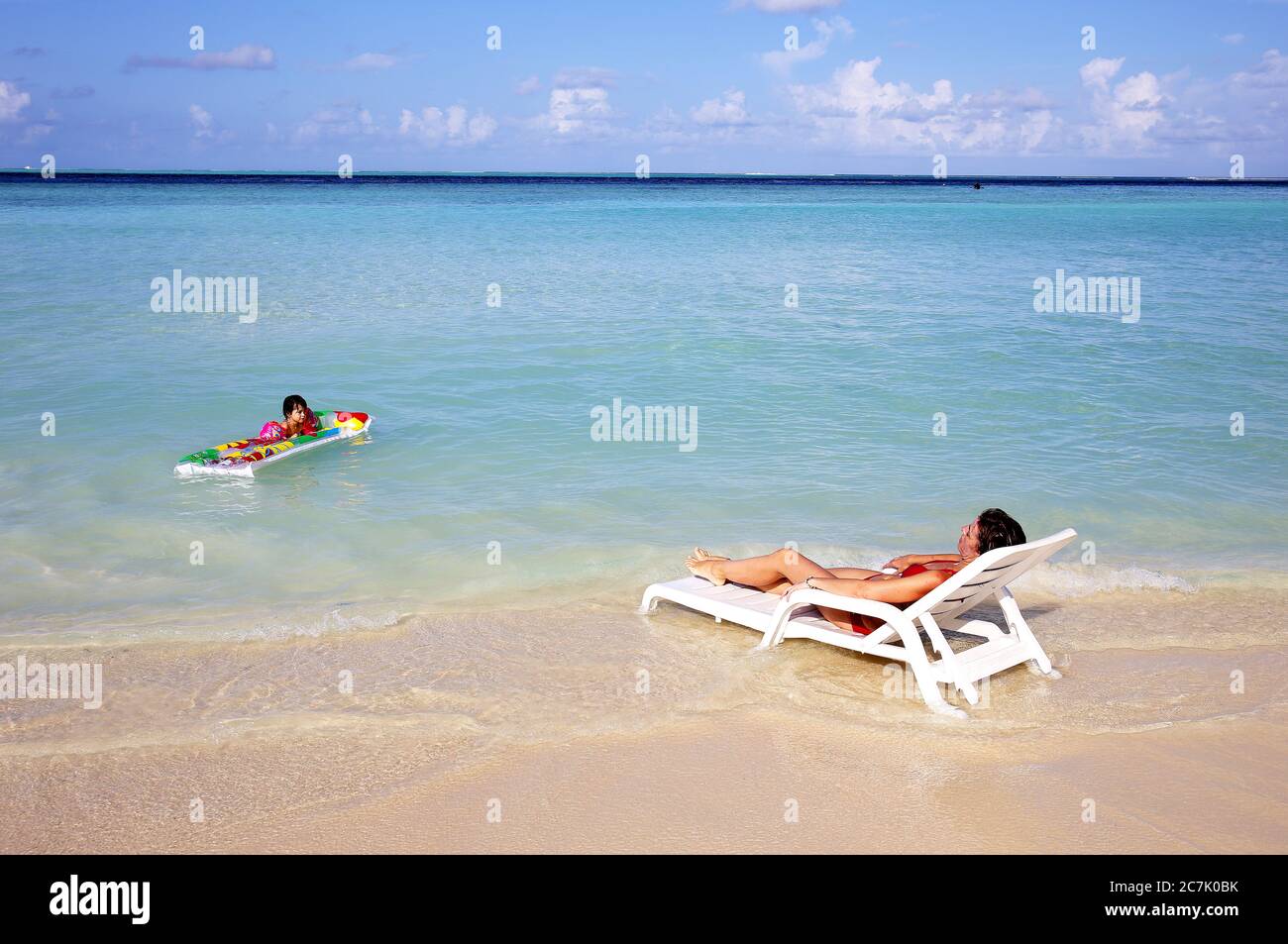 Mère bain de soleil, fille jouant avec un matelas gonflable sur la plage Gulhi, Maldives Banque D'Images