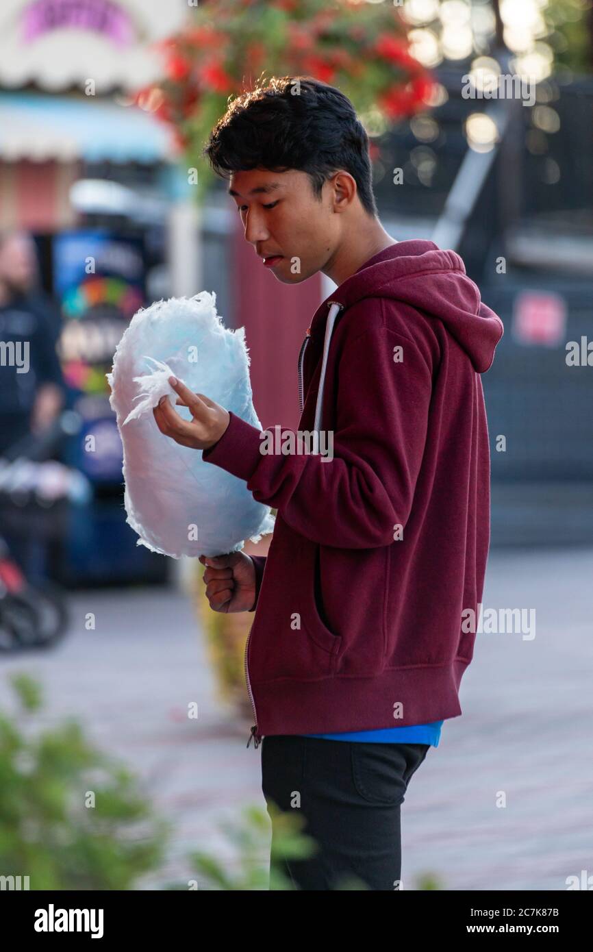 Jeune homme dans un sweat à capuche mangeant des bonbons en coton bleu Banque D'Images