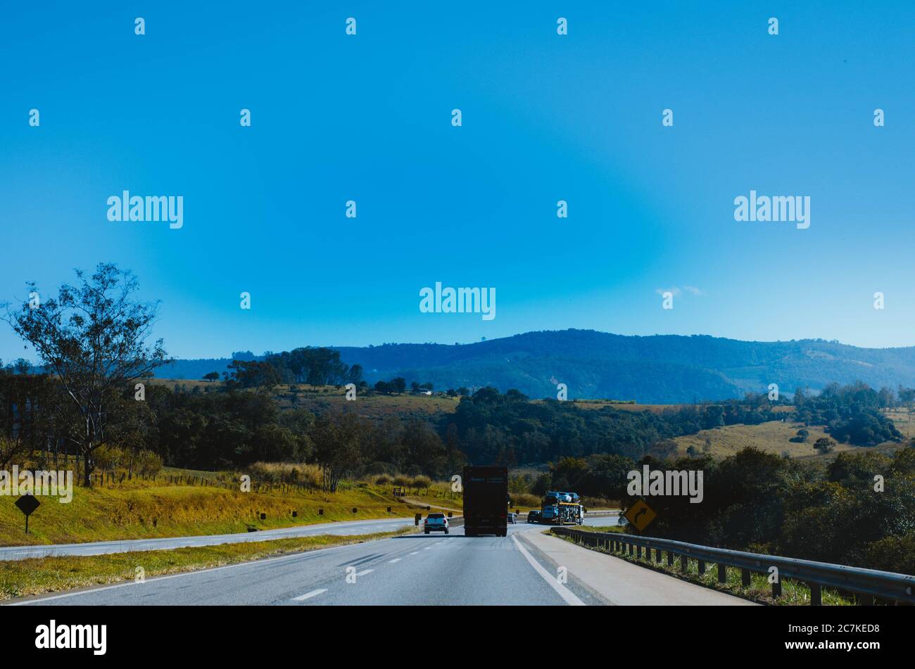 Vue spectaculaire sur l'autoroute Minas Gerais BR-381 entourée de verdure et de quelques véhicules à une distance dans un ciel propre dans l'après-midi. Banque D'Images