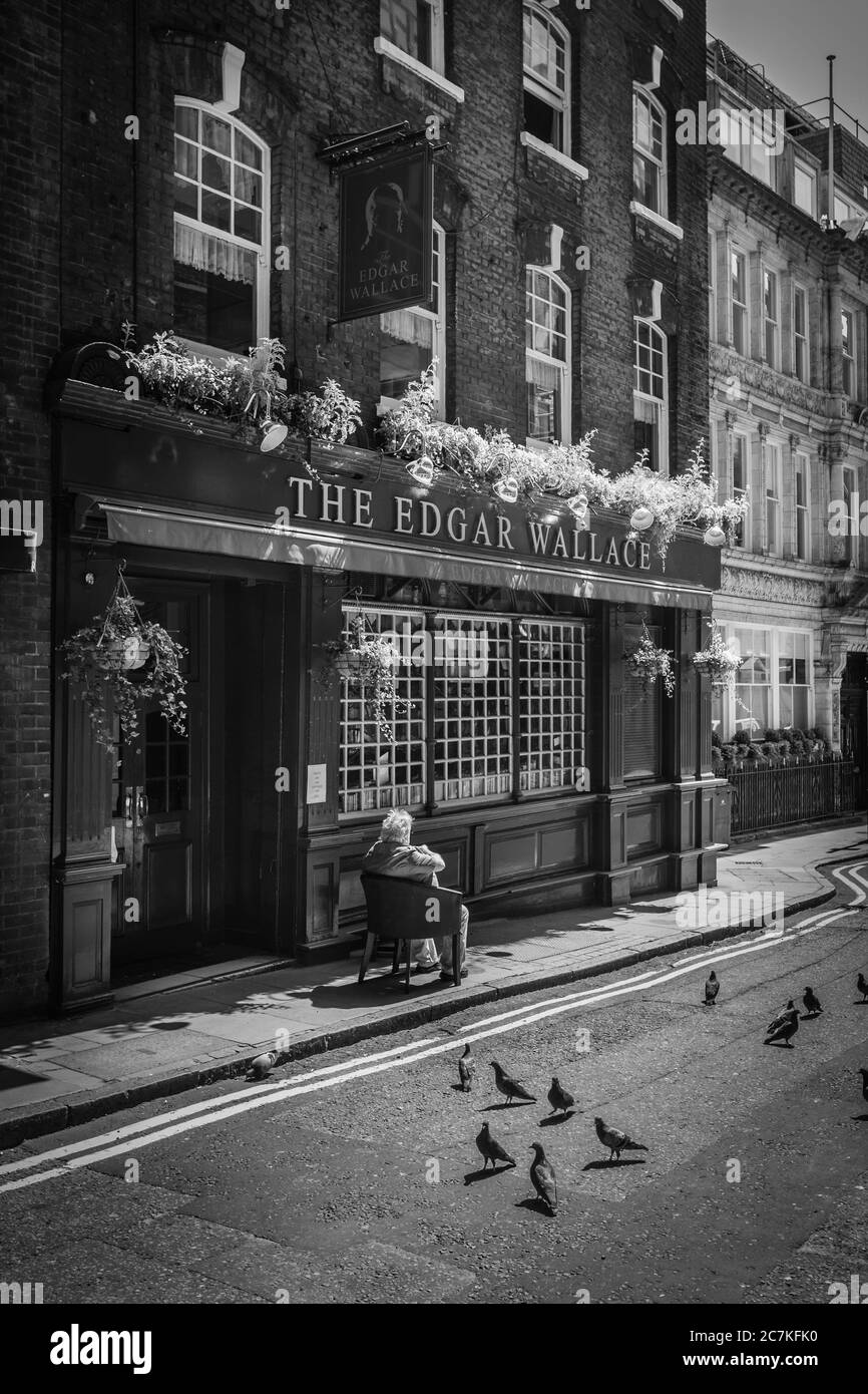 Un vieil homme s'assoit au soleil à l'extérieur du pub Edgar Wallace pendant son confinement à Londres pendant la pandémie du coronavirus. Banque D'Images