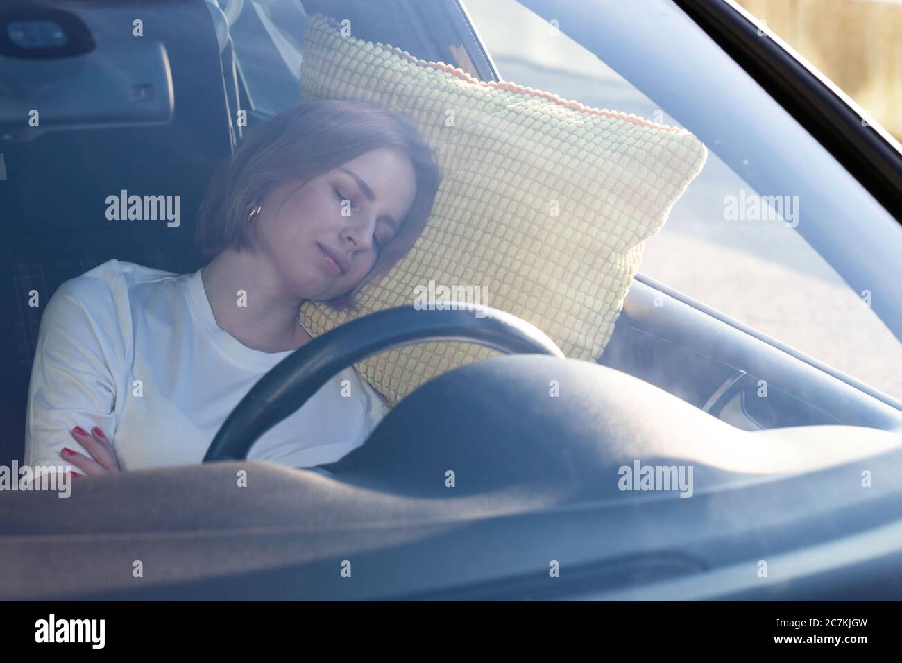 Jeune femme fatiguée, la conductrice s'est endormie sur un oreiller à l'intérieur de sa voiture, se reposant après de longues heures de conduite. Fatigue. Privation de sommeil. Banque D'Images