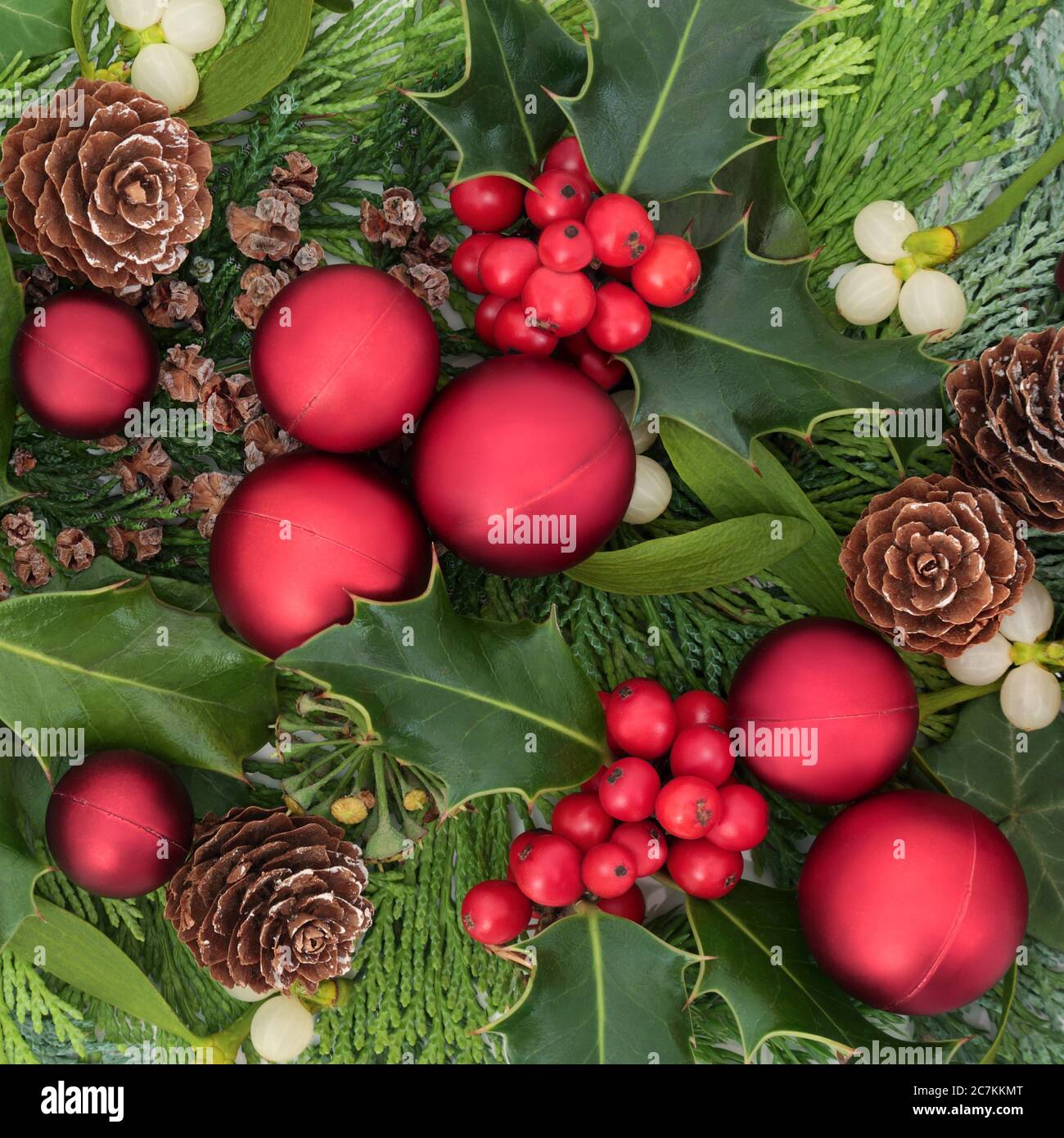 Noël composition festive pour les fêtes avec la verdure traditionnelle de l'hiver de houx, GUI, ivy, feuilles de cèdre, cônes de pin et boules rouges. Banque D'Images