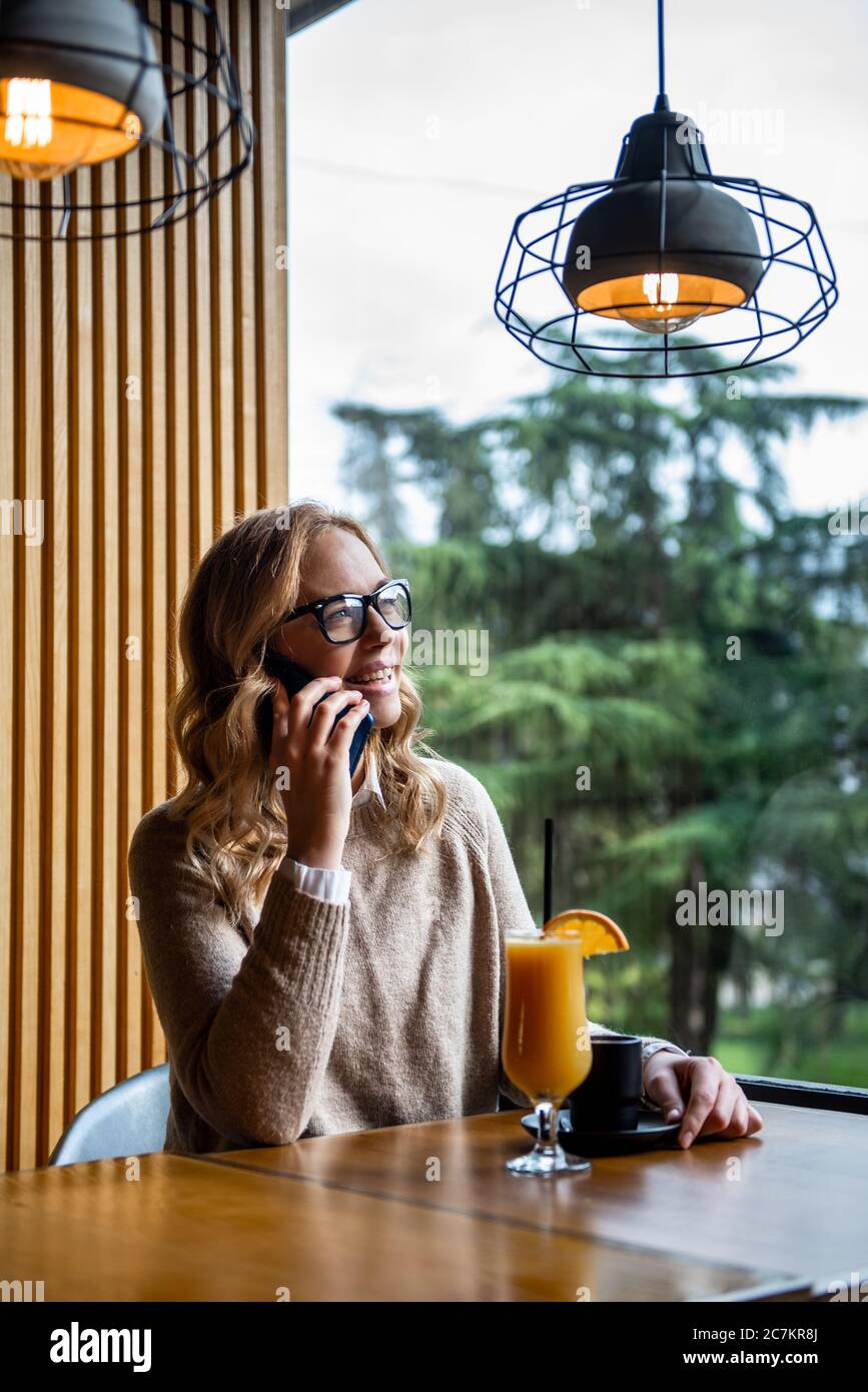 Charmante jeune femme appelant avec téléphone cellulaire alors qu'il était assis seul dans un café pendant le temps libre, belle femelle avec sourire mignon avoir parler Banque D'Images