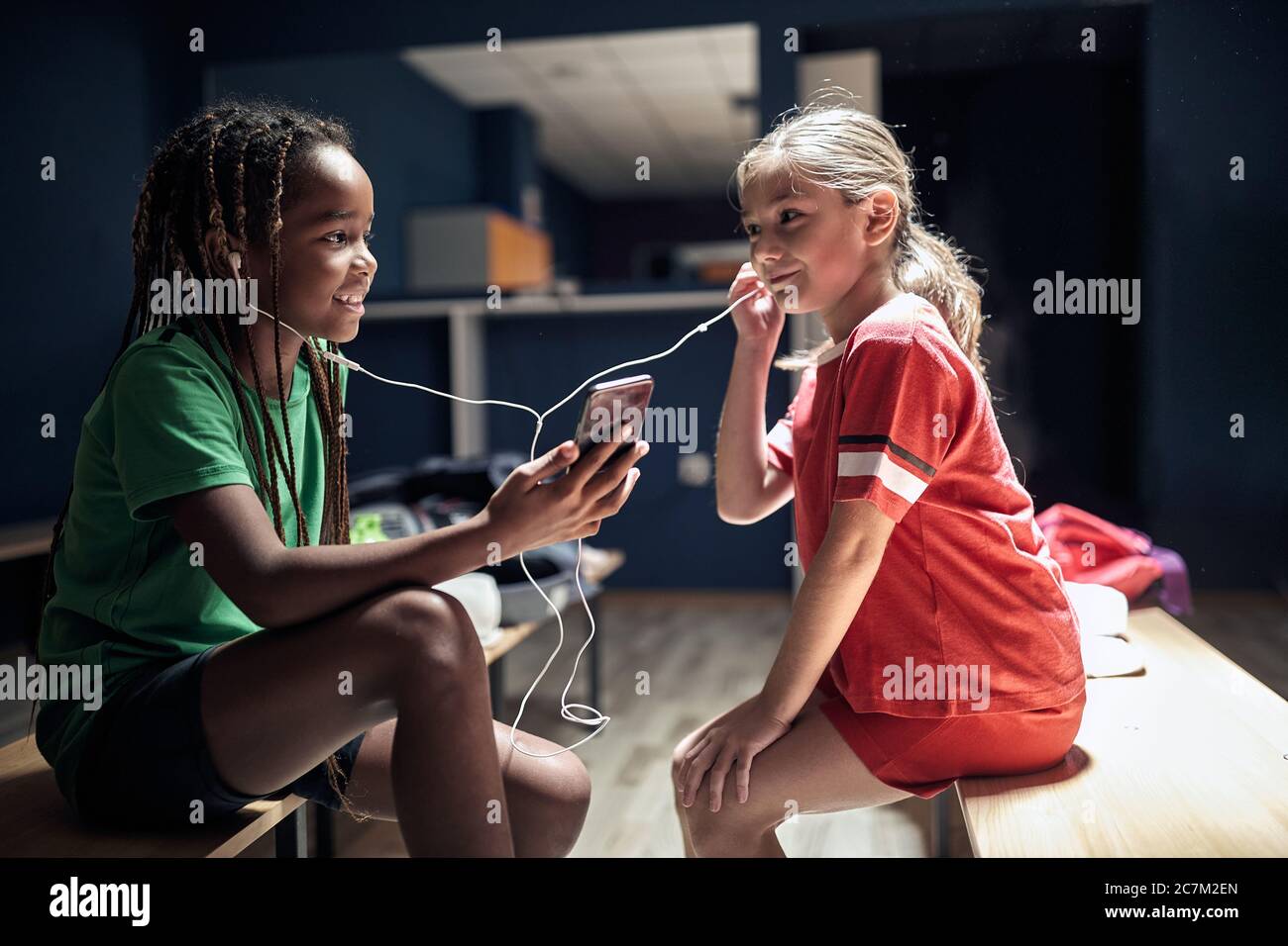 Deux filles souriantes de football joueur avant l'entraînement écouter de la musique sur téléphone dans le vestiaire. Banque D'Images