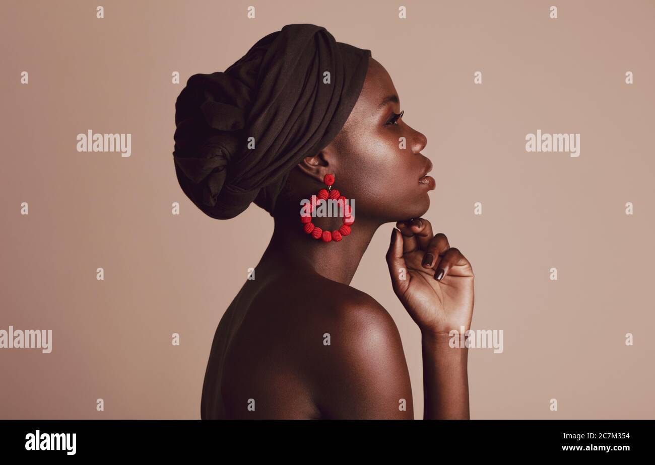 Vue latérale d'une femme portant un turban noir sur fond beige. Modèle africain féminin avec belle peau posant en studio. Banque D'Images