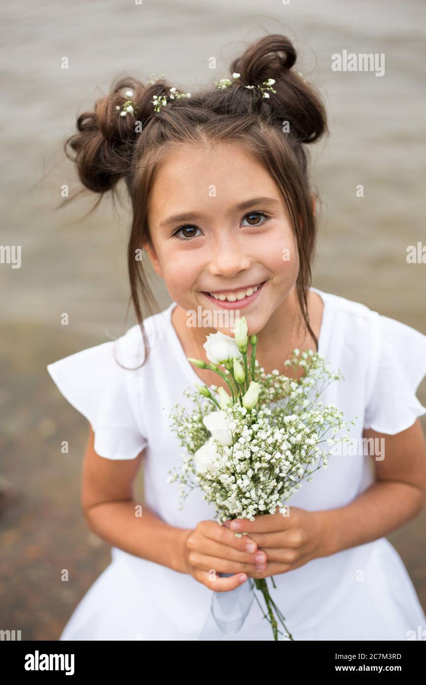 une fille tient un bouquet de fleurs blanches sur un fond flou.cheveux foncés, fleurs blanches dans ses mains, robe blanche Banque D'Images