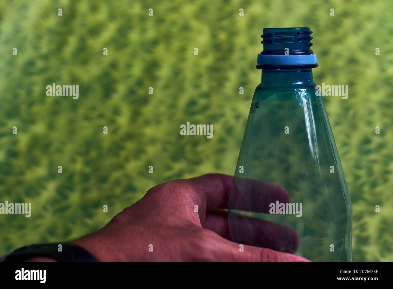 Gros plan de la main d'un homme portant un plastique bleu bouteille avec fond vert Banque D'Images