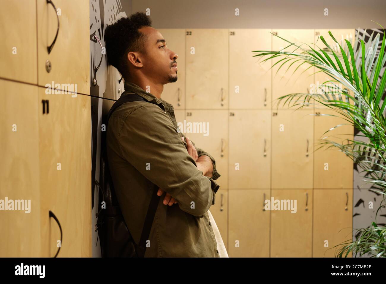 Vue latérale d'un jeune homme afro-américain élégant et décontracté, assis dans un vestiaire seul Banque D'Images