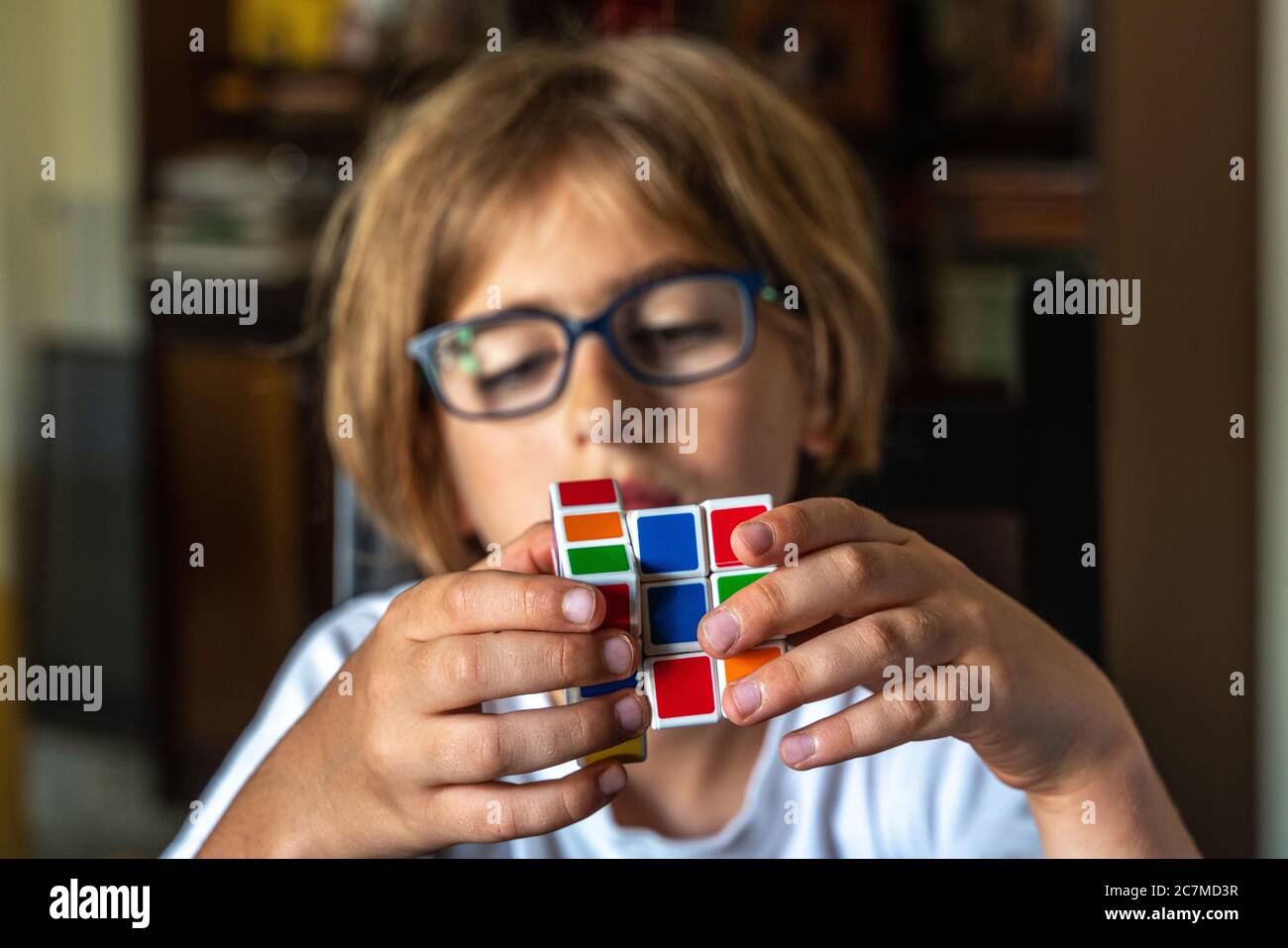Enfant avec des lunettes essayant de résoudre le cube de Rubik Banque D'Images