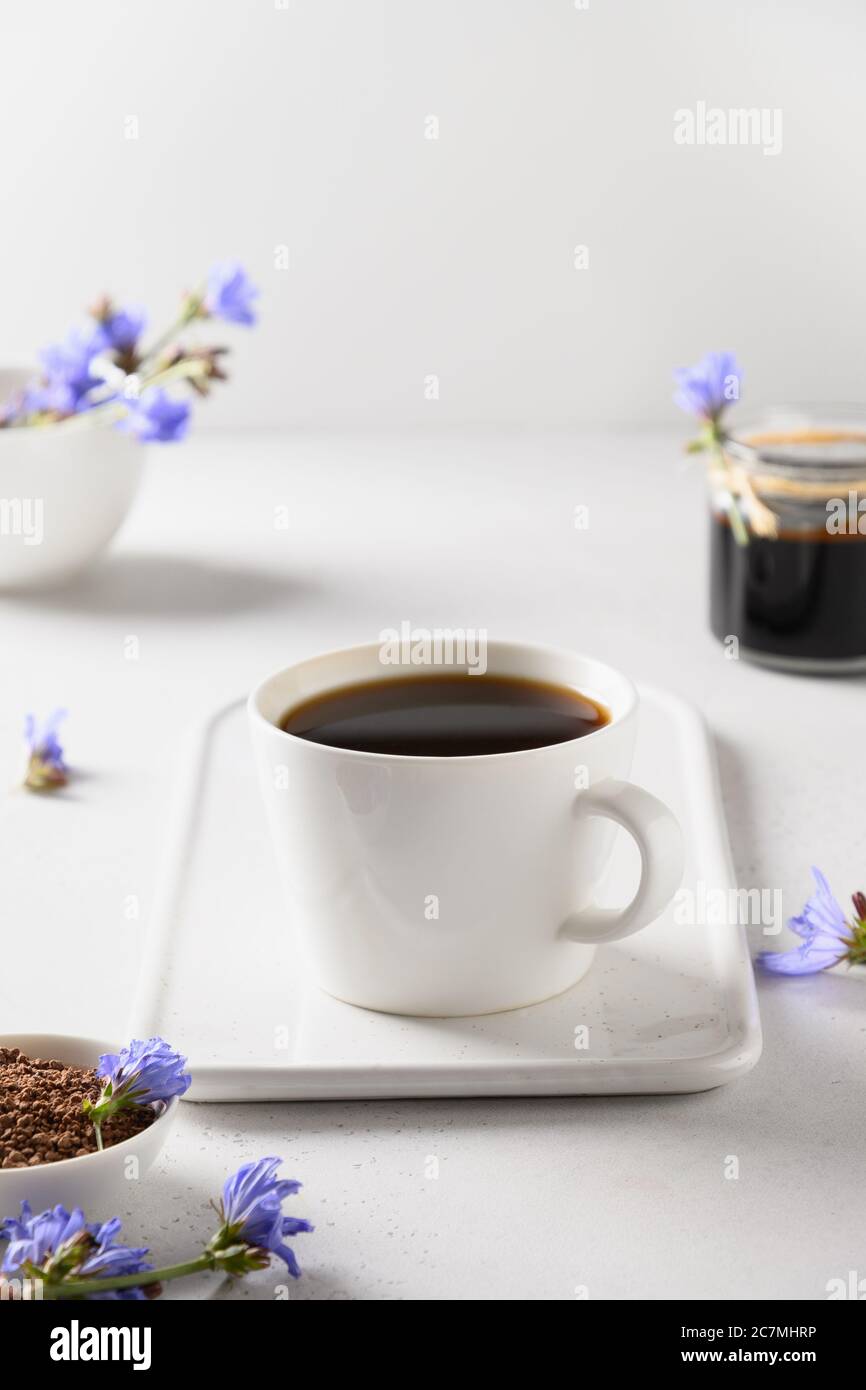Café racine de chicorée en tasse et fleurs fraîches. Avantages pour la santé. Format vertical. Gros plan. Banque D'Images