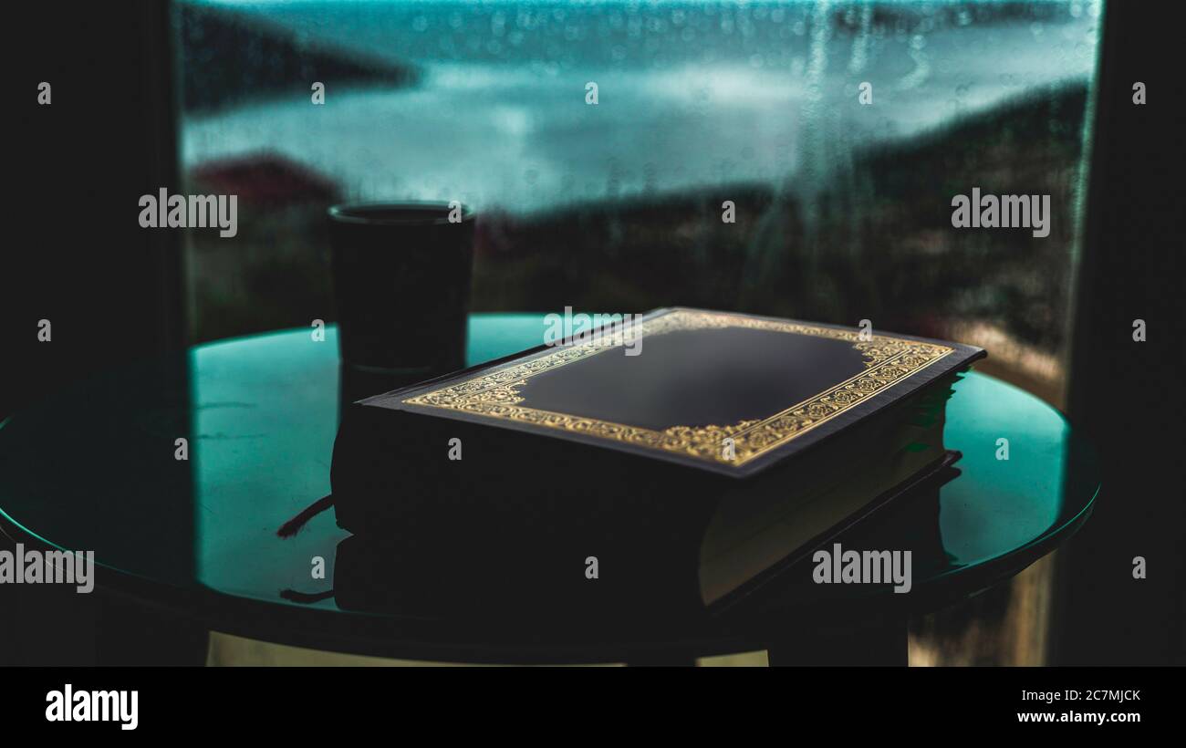 Photo d'un livre islamique et d'un café sur une table dans une maison au bord de la mer avec une belle mer sur le fond, par un jour pluvieux Banque D'Images
