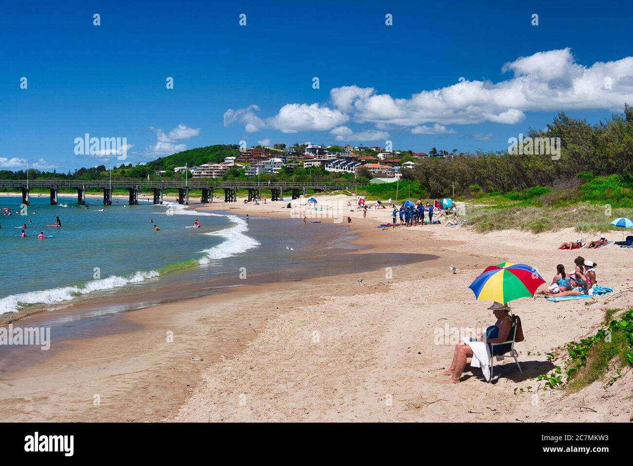 Une des plages de Coffs Harbour, au milieu de la côte de Nouvelle-Galles du Sud, en Australie. Personne sous un parapluie coloré au premier plan Banque D'Images