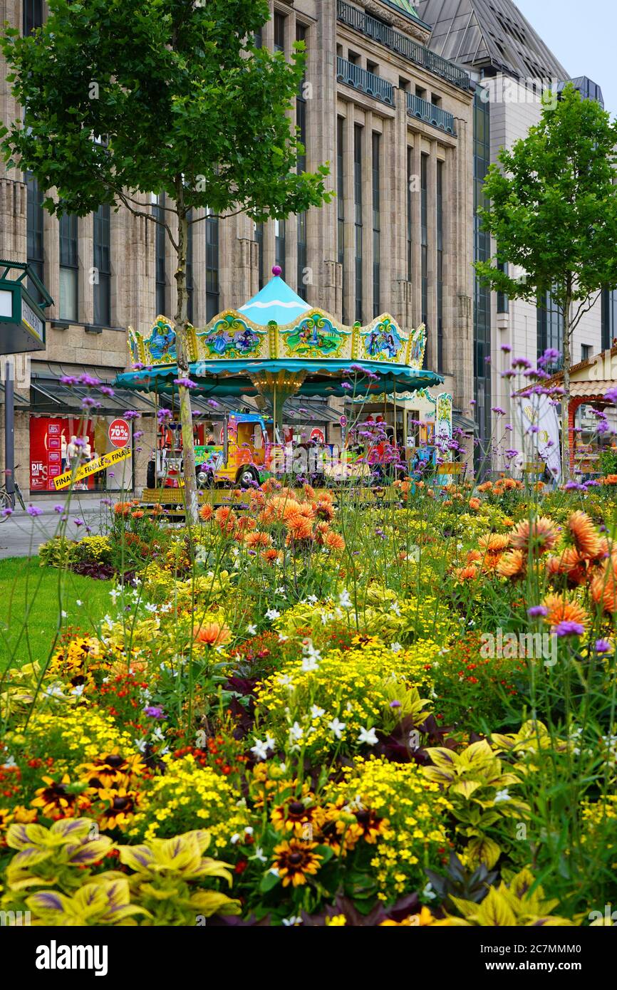 Carrousel nostalgique en face du bâtiment historique du grand magasin « Kaufhof » avec des fleurs d'été colorées en premier plan. Banque D'Images