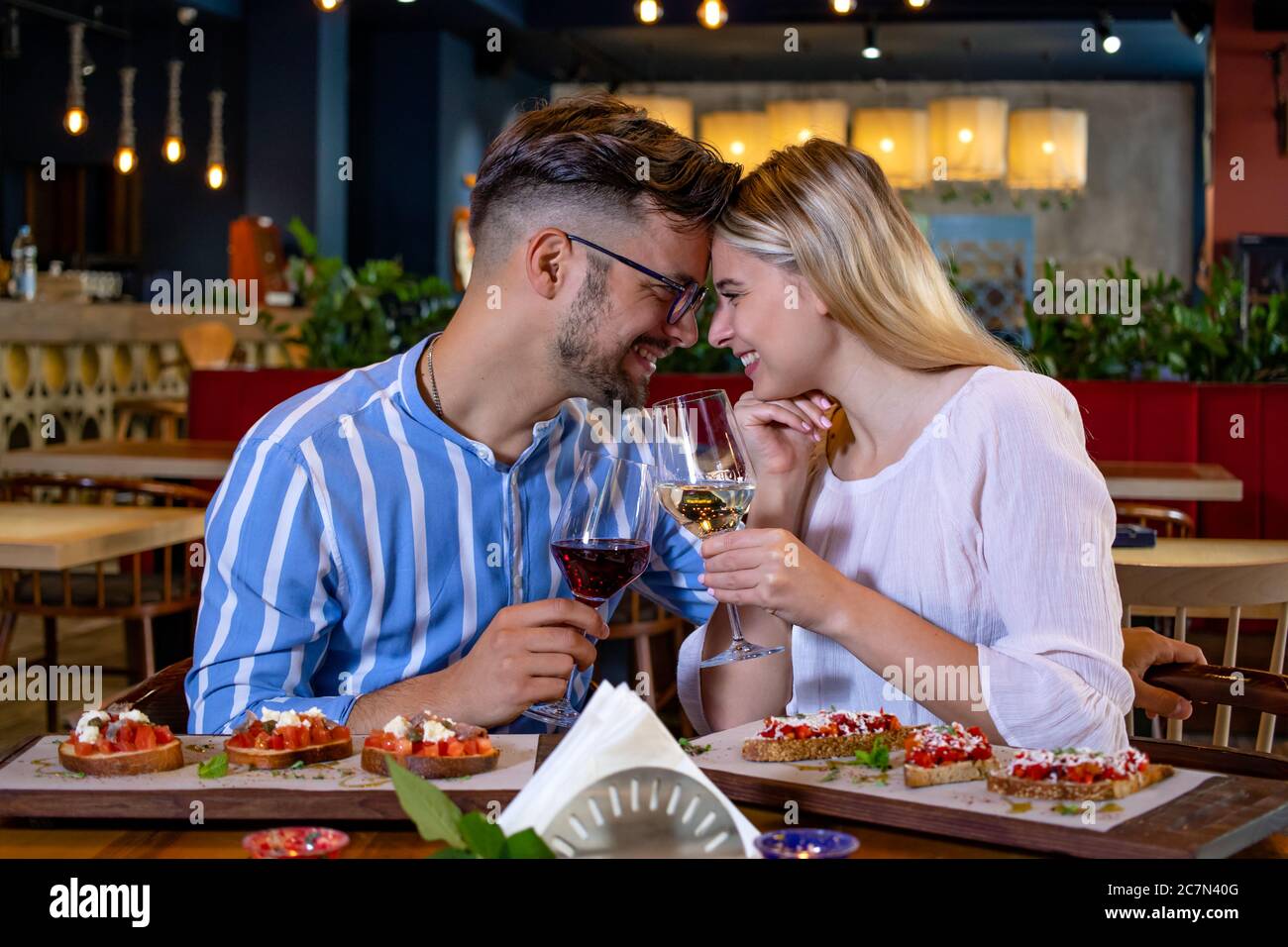 Un couple joyeux et romantique, amoureux, boit du vin, souriant et toaster au dîner dans un magnifique restaurant chic. Banque D'Images