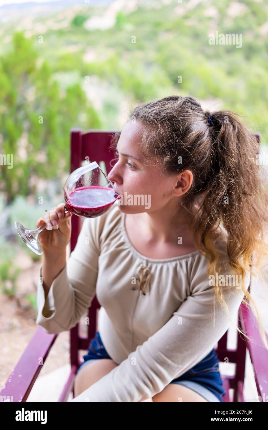 Femme assise à l'extérieur dans une chaise buvant un verre de vin rouge ou de jus de canneberge dans le jardin du désert de Santa Fe vue verticale Banque D'Images