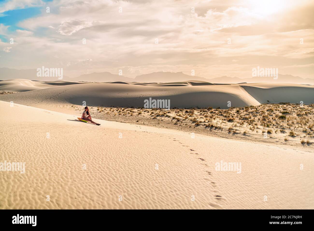 Jeune fille sur le sable dans les dunes de sable blanc monument national au Nouveau-Mexique assis sur un traîneau à disques pour glisser sur la colline pendant le coucher du soleil de ton vintage Banque D'Images