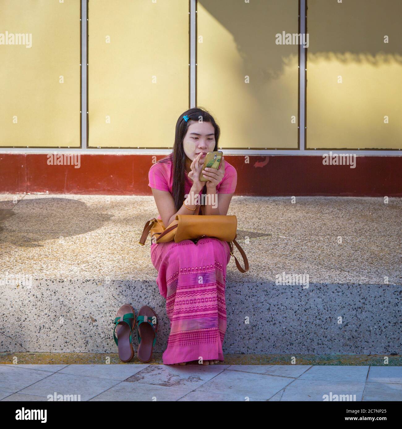 Une jeune femme est assise sur un trottoir regardant son téléphone cellulaire à la Pagode Shwedagon à Yangon, au Myanmar Banque D'Images Une jeune femme est assise sur un trottoir regardant son téléphone cellulaire à la Pagode Shwedagon à Yangon, au Myanmar Banque D'Images