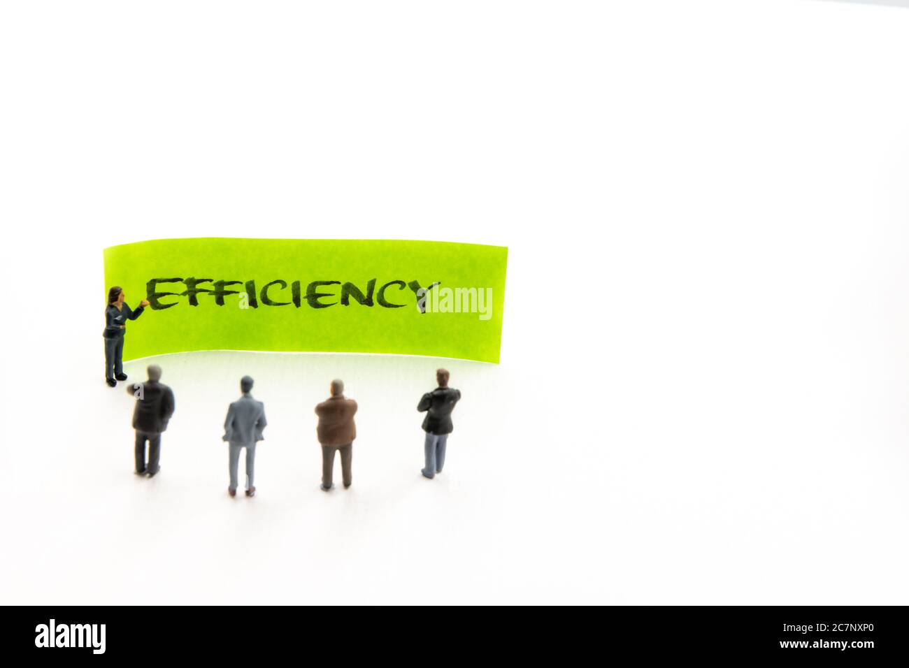 Rencontre avec des figurines miniatures posées comme des hommes d'affaires se tenant autour de post-it note avec efficacité message manuscrit en arrière-plan, minimaliste a Banque D'Images