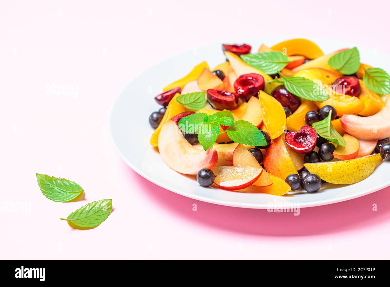 Salade de fruits avec baies dans une assiette blanche, fond rose. Concept alimentaire végétalien sain. Banque D'Images