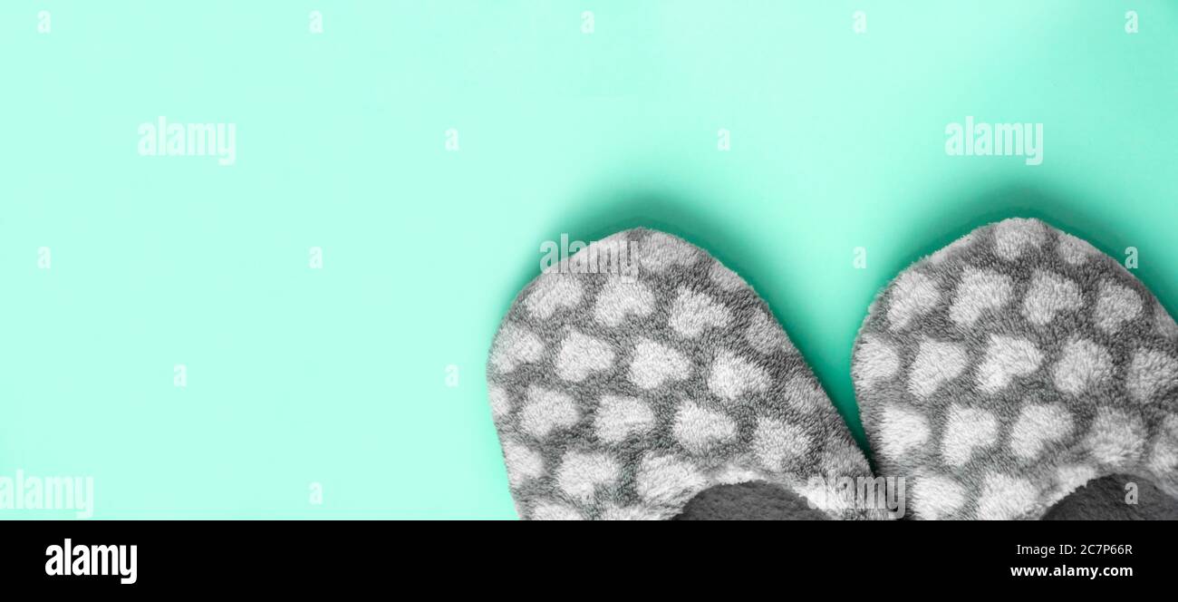 Paire de pantoufles grises moelleuses avec coeurs blancs sur fond de menthe néo. Chaussures confortables et chaudes. Maison douce, détente, agrément, concept d'hygge Banque D'Images
