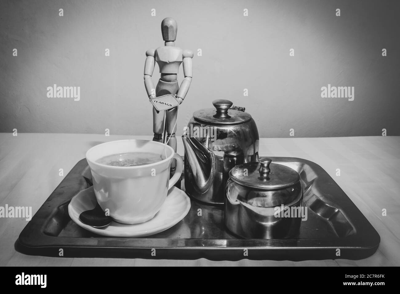 Mannequin humain en bois posé avec une tasse de thé sur un plateau argenté, une théière et une sucrière. Banque D'Images