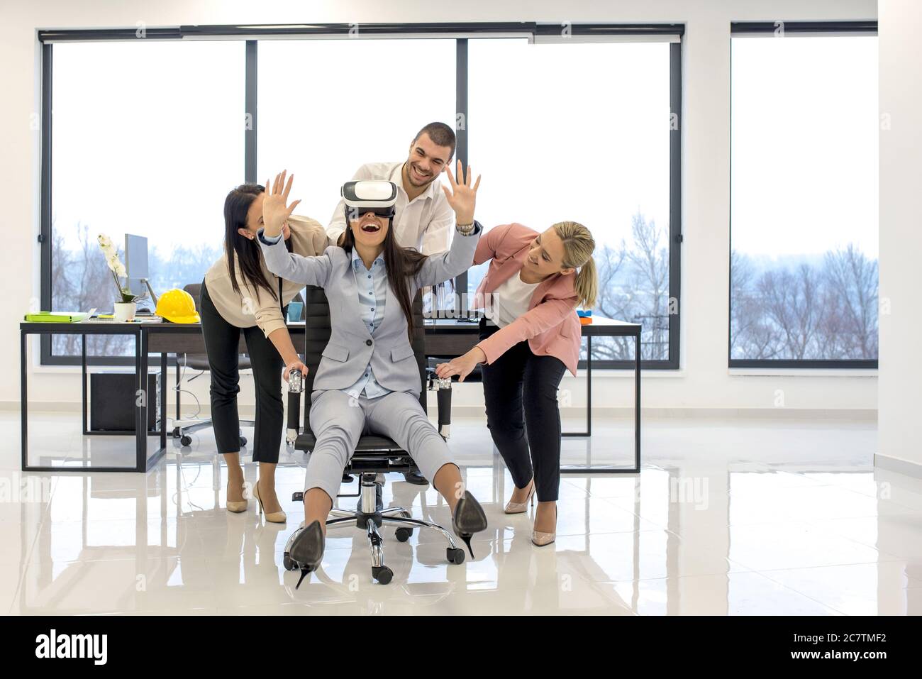 Des collègues se sont rassemblés autour d'une femme portant un casque de réalité virtuelle assis sur une chaise Banque D'Images