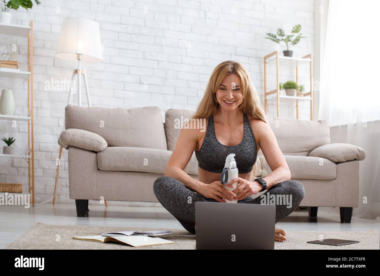 Le coach en ligne a une discussion en ligne après la formation avec les abonnés. Femme assise sur le sol, regarde l'ordinateur portable Banque D'Images