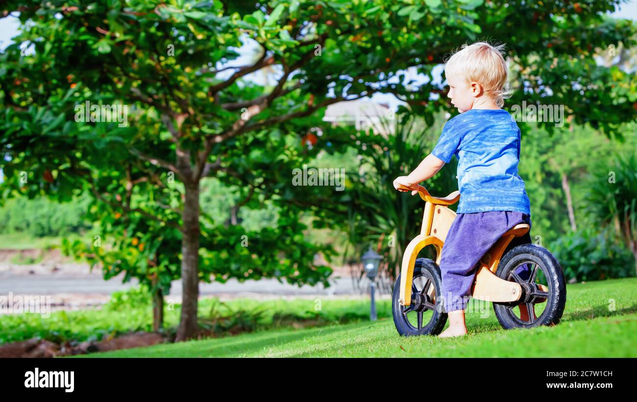 2 - 3 ans joyeux garçon à cheval sur un vélo d'équilibre en bois (vélo de course). Bonne sensation pieds nus, enfant qui apprend à se mettre à la roue, garde l'équilibre sur le vélo d'entraînement Banque D'Images