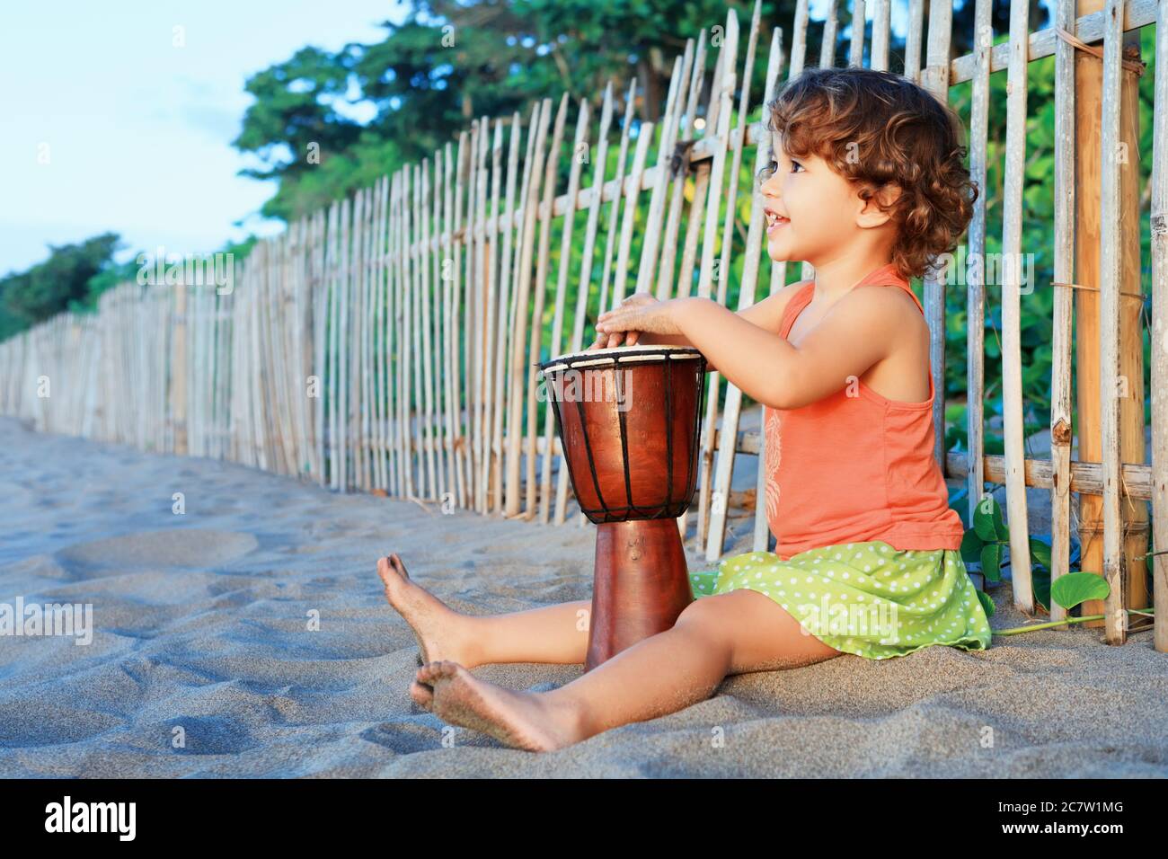 Petite fille de bébé heureux jouer de la musique ethnique sur le djembe  africain traditionnel tambour main, en appréciant le coucher de soleil sur  la plage de l'océan. Enfants mode de vie