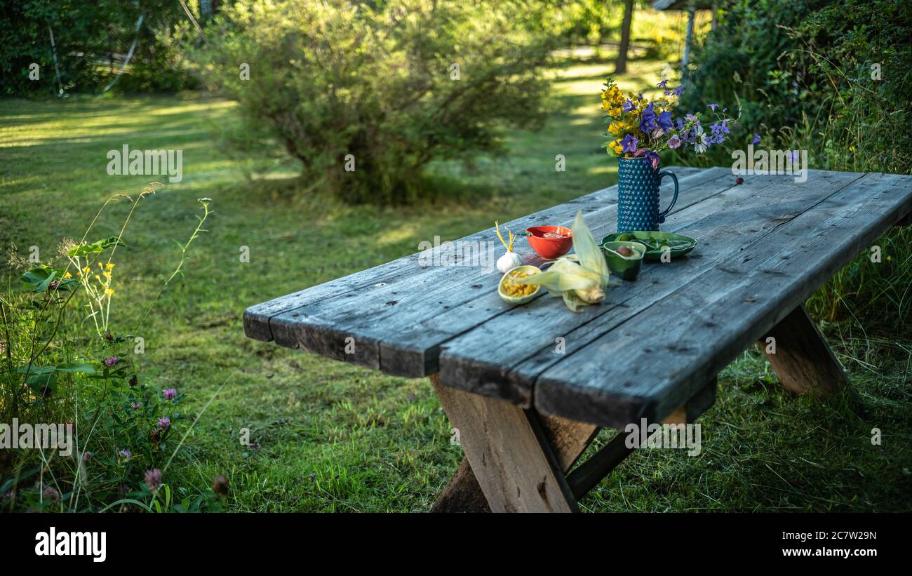 Jardin avec table en bois de vieux planches dans le pays avec des fleurs et préparation avec des légumes lors d'une belle journée d'été en Suède Banque D'Images
