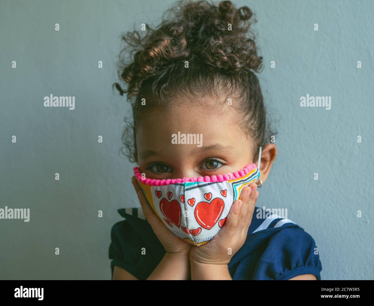 Une petite fille avec un masque avec les coeurs regarde l'appareil photo et embrassant son visage Banque D'Images