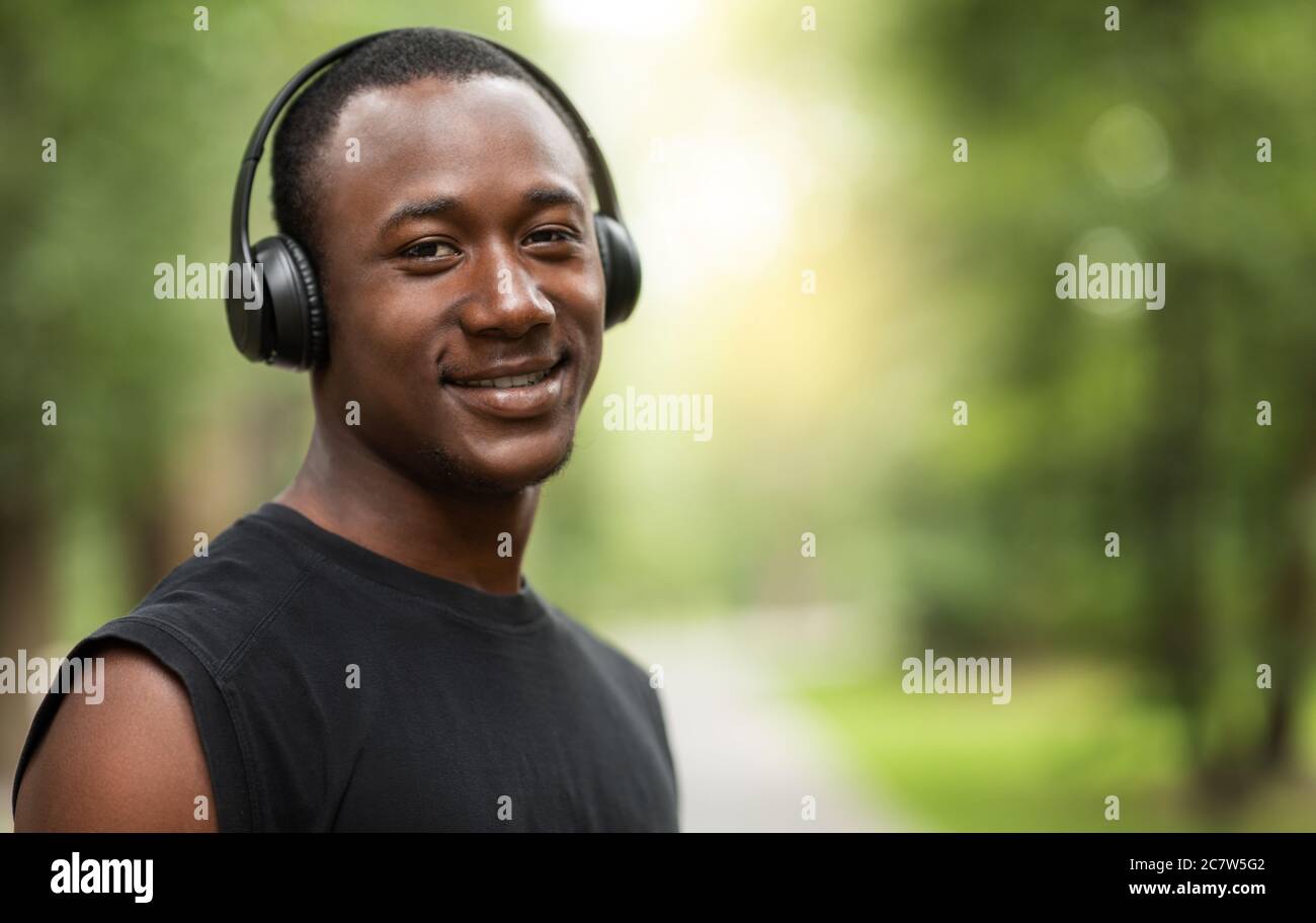 Portrait d'un homme noir souriant avec casque sans fil, entraînement en extérieur Banque D'Images