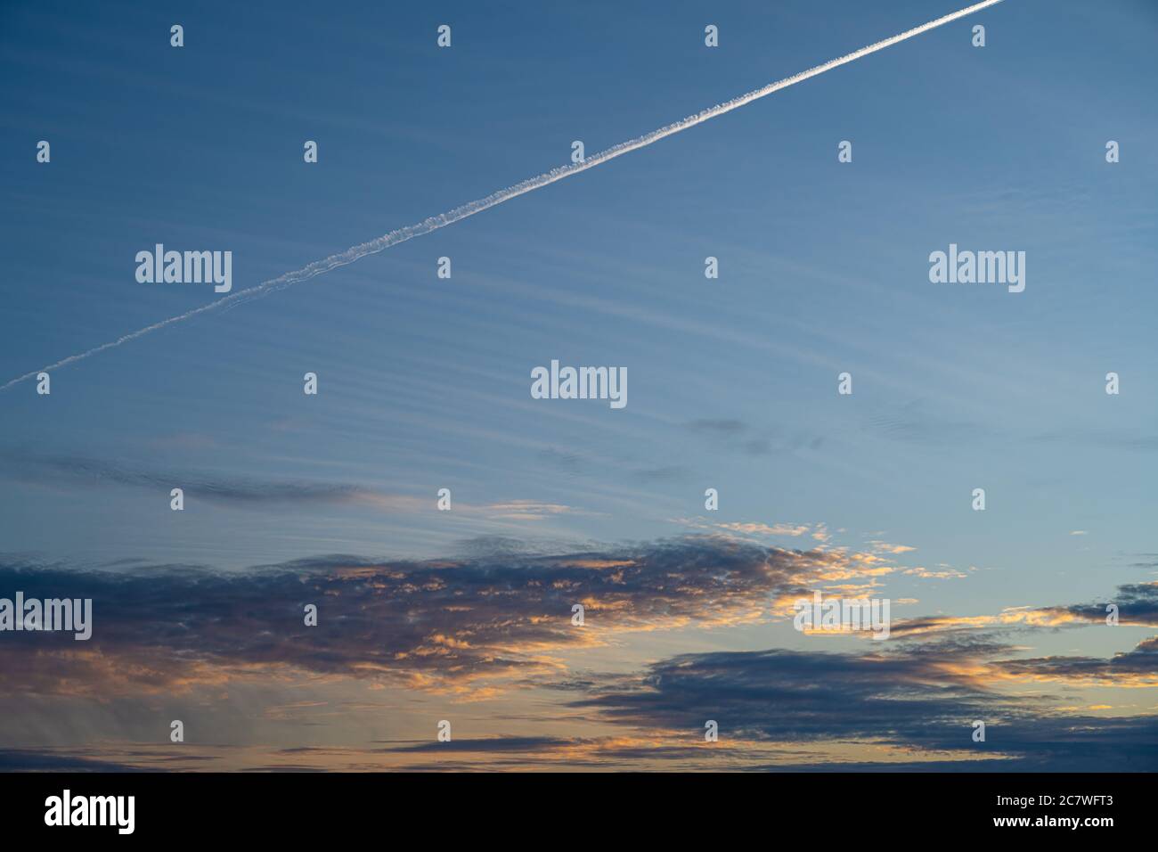 Un avion laisse une ligne de vapeur blanche sur un magnifique ciel bleu de coucher de soleil. Ciel bleu, nuages sombres et coucher de soleil orange Banque D'Images