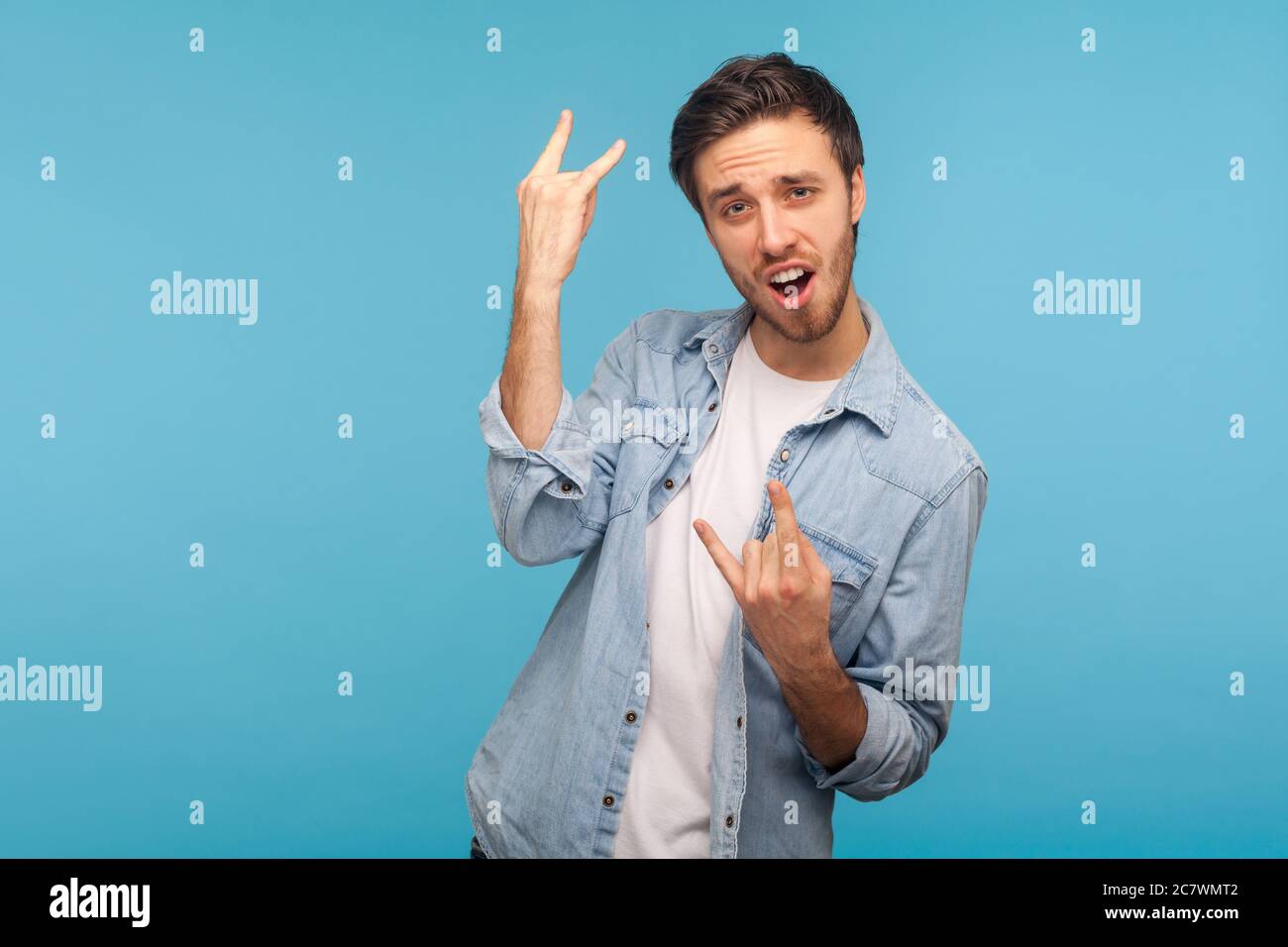 Oui, c'est fou ! Portrait d'un homme enthousiaste dans une chemise en denim de travailleur montrant le mouvement de la main de rock et de rouleau et criant dans le plaisir, faisant des cornes de diable Banque D'Images