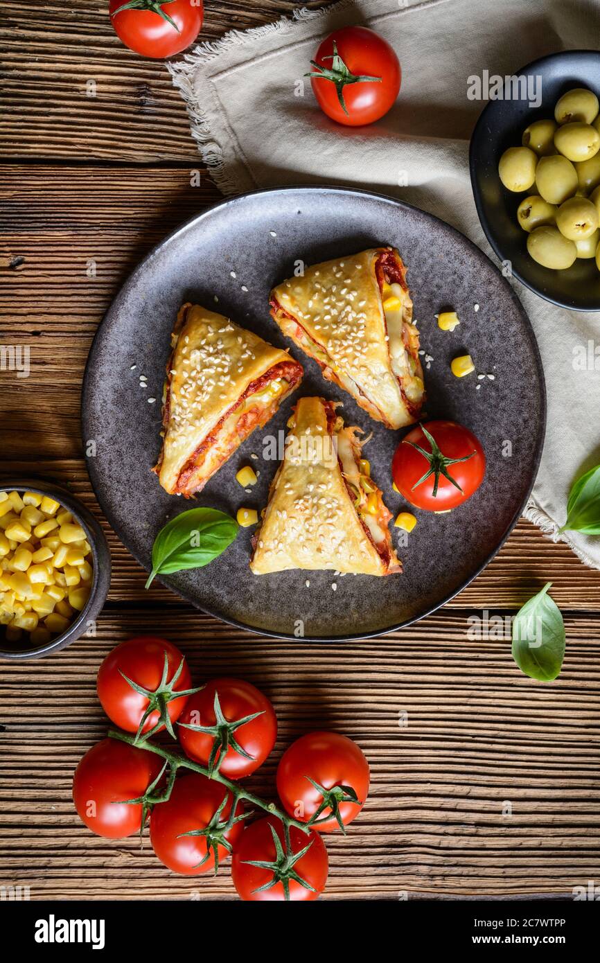 Délicieux feuilletés feuilleté pizza triangle rouleaux farcis avec sauce tomate, jambon, fromage, maïs, olives et arrosé de graines de sésame Banque D'Images
