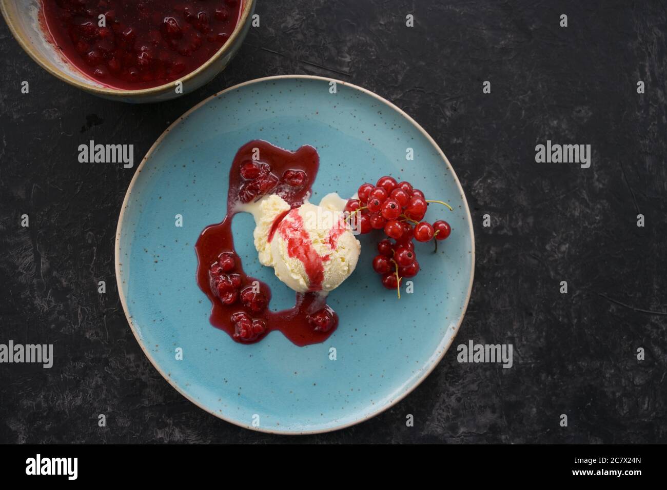 Glace à la vanille avec cassis rouge et sauce à la gelée de fruits sur une assiette bleue, fond sombre avec espace de copie, vue en grand angle depuis le dessus, mise au point sélectionnée Banque D'Images