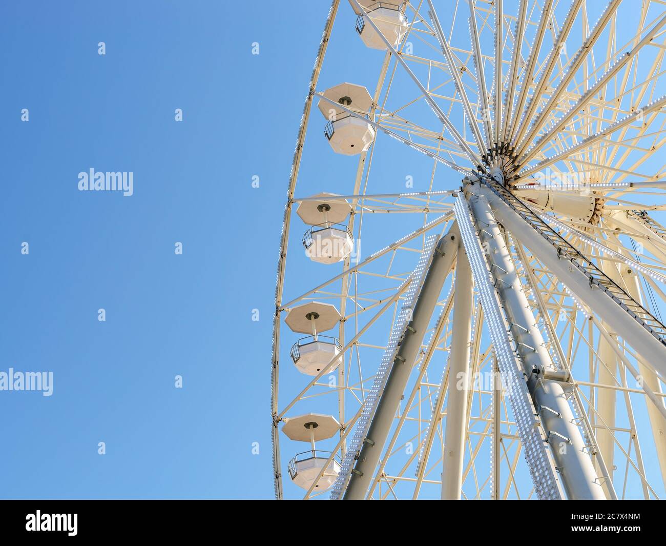 Attraction de la roue blanche de ferris illuminée avec des lumières blanches vives contre le ciel bleu clair lors d'une journée ensoleillée d'été. Divertissement pendant les vacances d'été. Banque D'Images