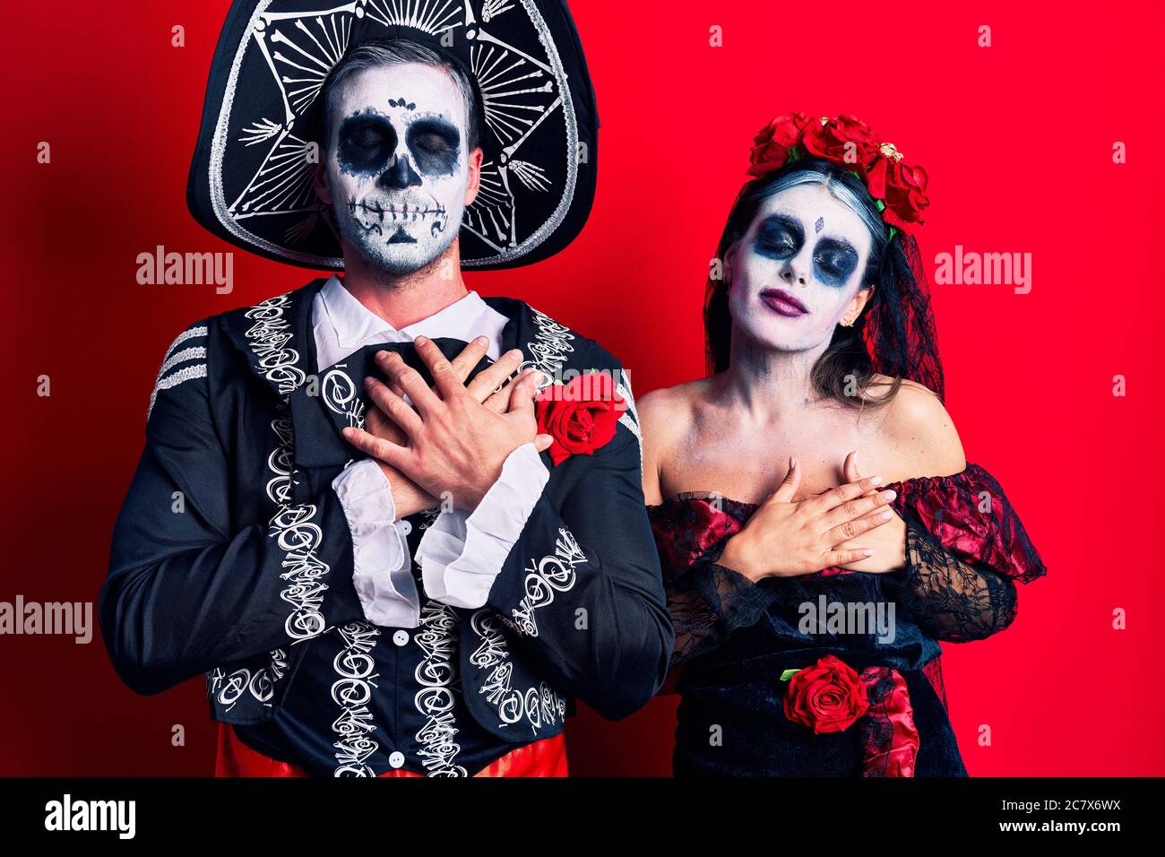 Jeune couple portant le costume mexicain du jour mort sur le rouge souriant  avec les mains sur la poitrine avec les yeux fermés et geste reconnaissant  sur le visage Photo Stock -