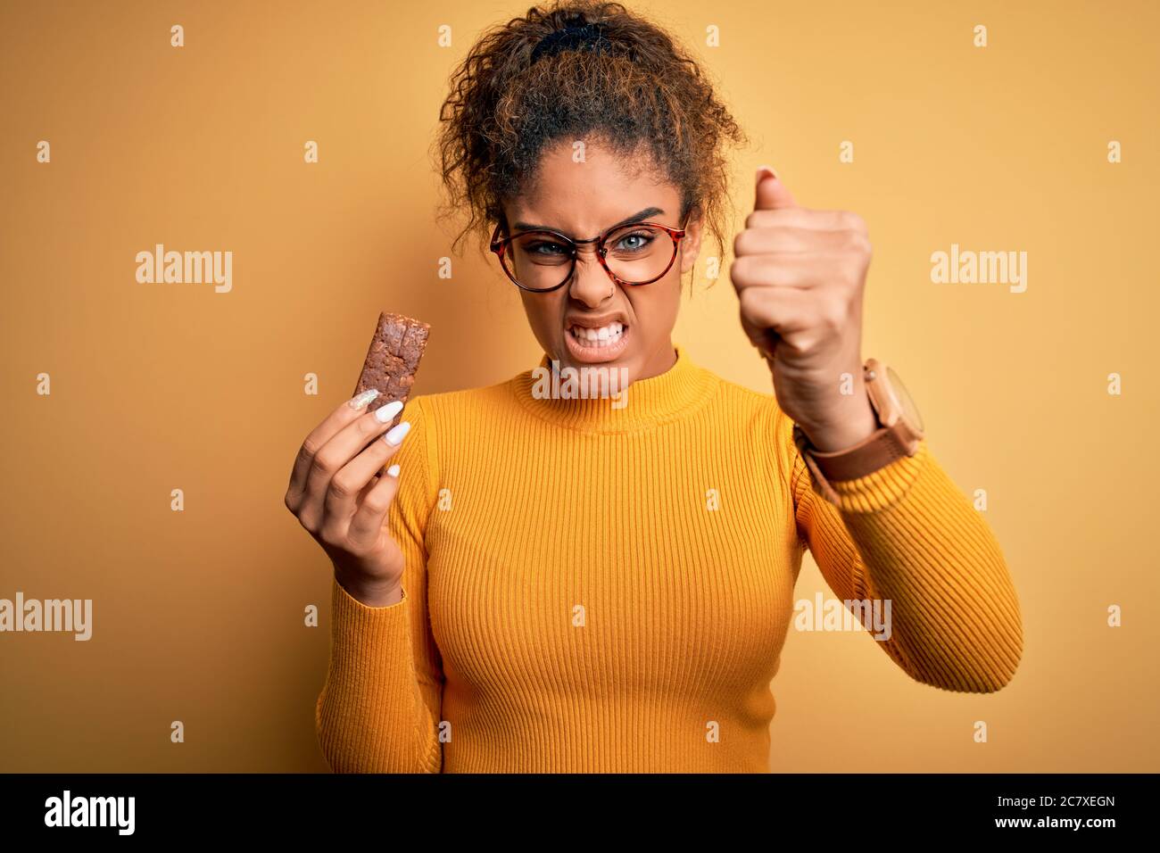 Jeune afroaméricaine africaine manger une barre de protéines énergétiques de céréales sur fond