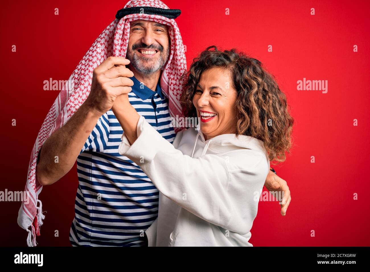 Un beau couple d'âge moyen porte un foulard arabe et un sweat-shirt  souriant heureux et confiant. Se tenant avec le sourire sur le visage  embrassant sur isolé rouge b Photo Stock -