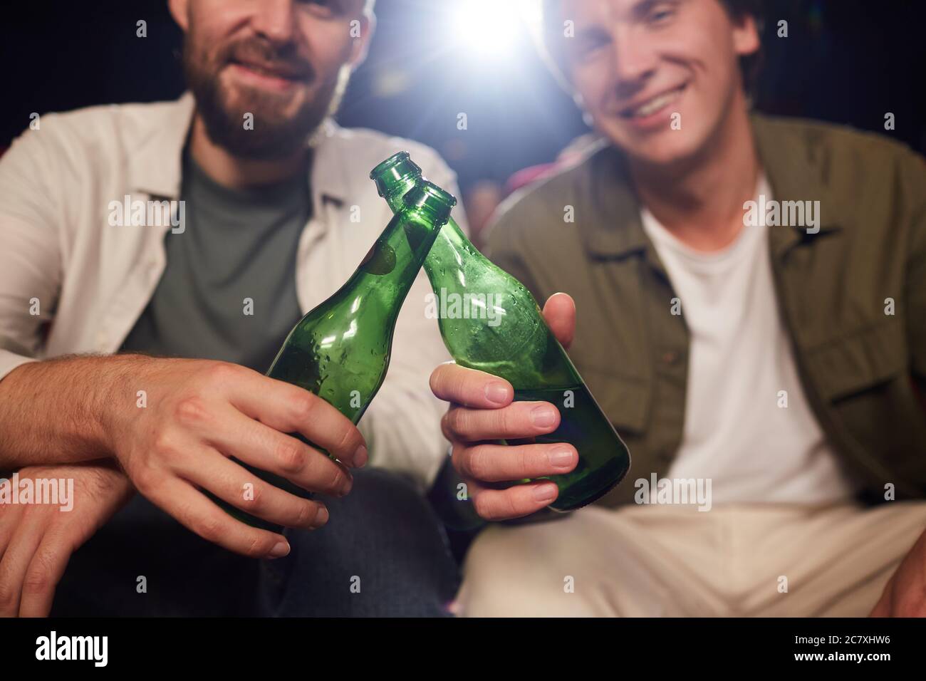 Gros plan de deux amis souriants et clinquant des bouteilles de bière tout en regardant un film au cinéma, dans l'espace de copie Banque D'Images