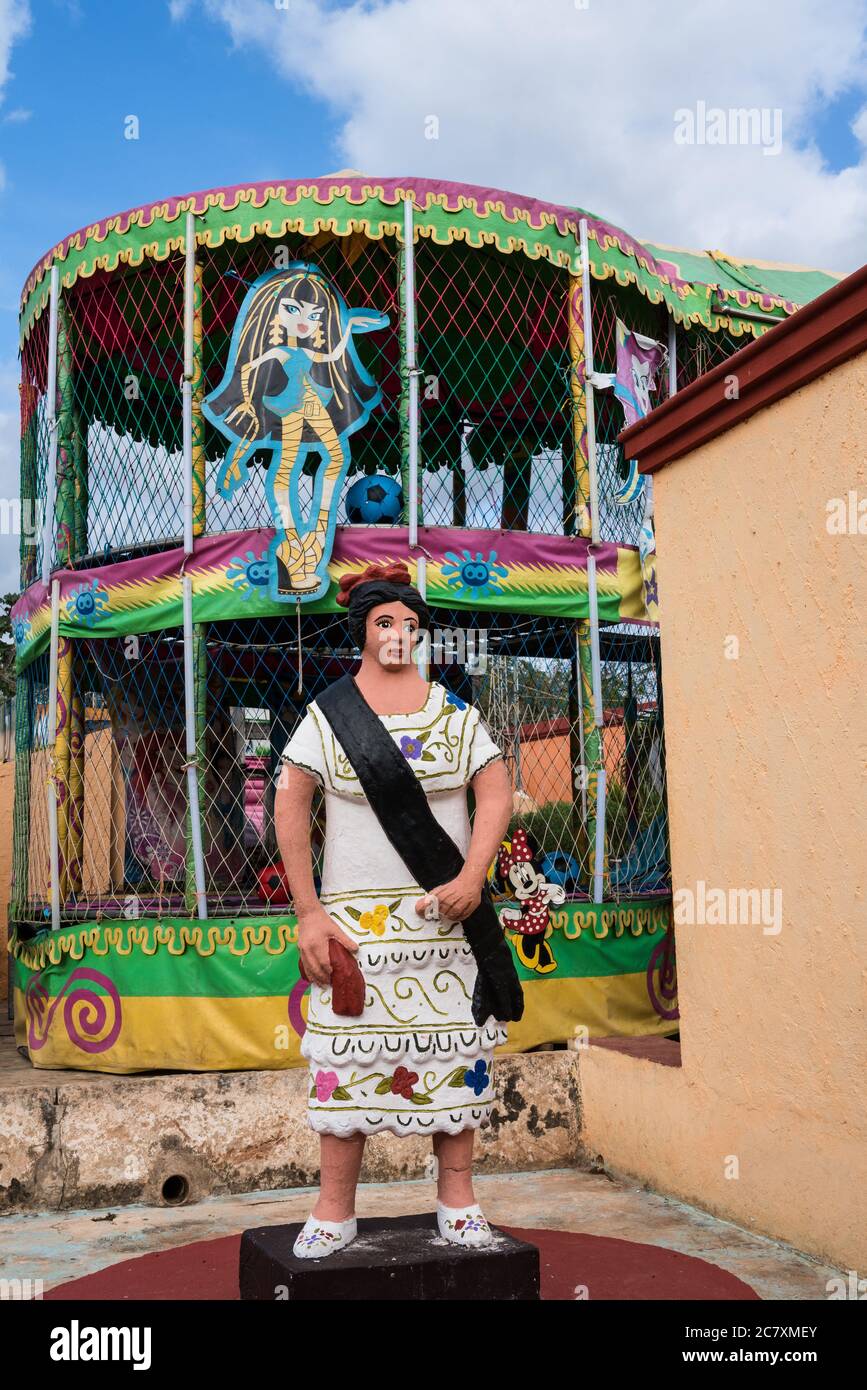 Ancien et nouveau. Statue d'une femme en robe traditionnelle typique à Santa Elena, Yucatan, Mexique. Derrière elle se cache un personnage de dessin animé moderne. Banque D'Images